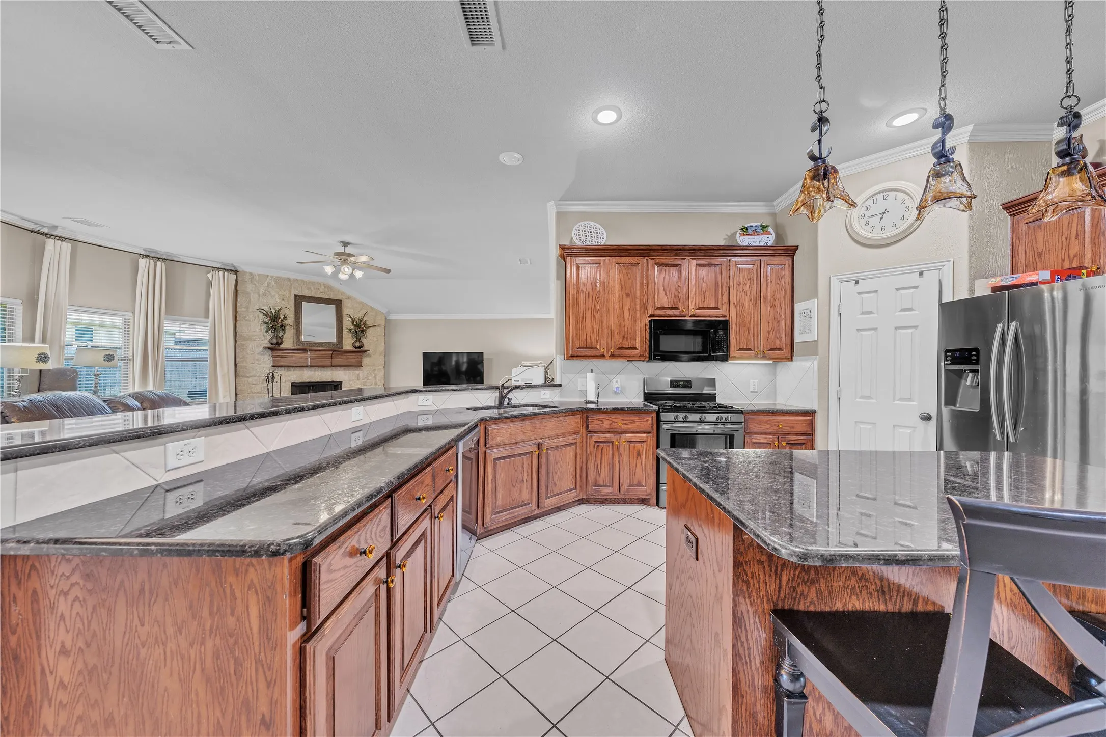 Kitchen featuring a large central island with granite countertops, stainless steel appliances, wood cabinetry, and white tile flooring