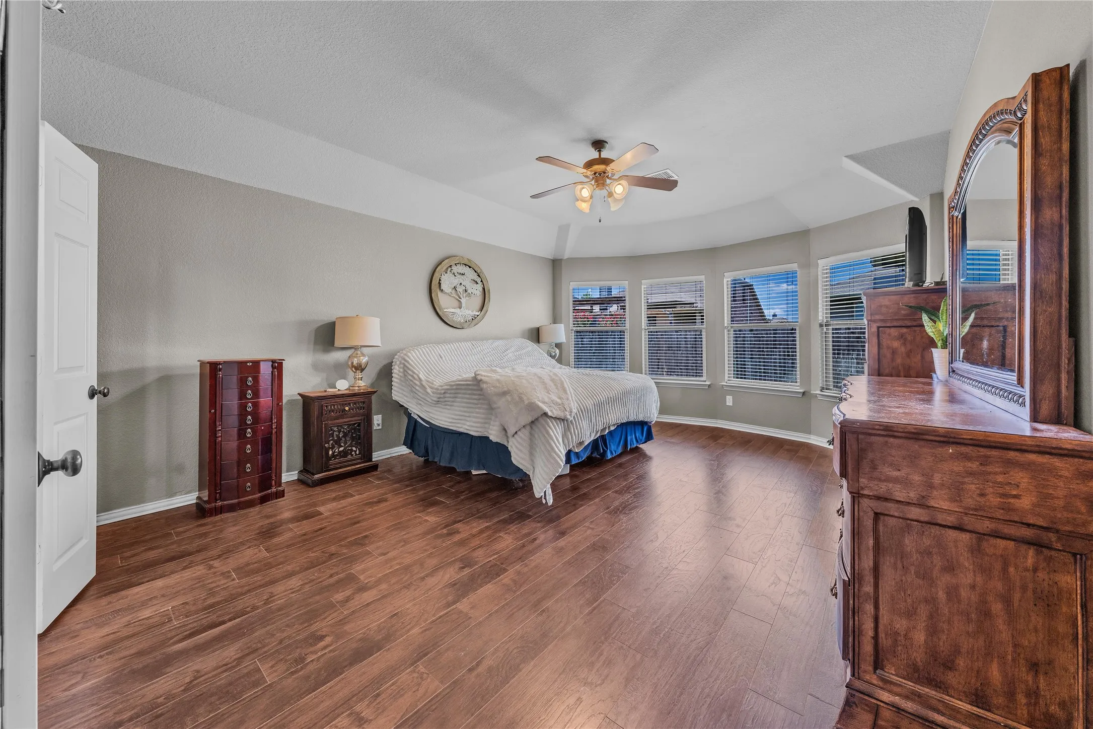 Spacious room featuring wood-finish flooring, a tray ceiling, and a ceiling fan with integrated lighting