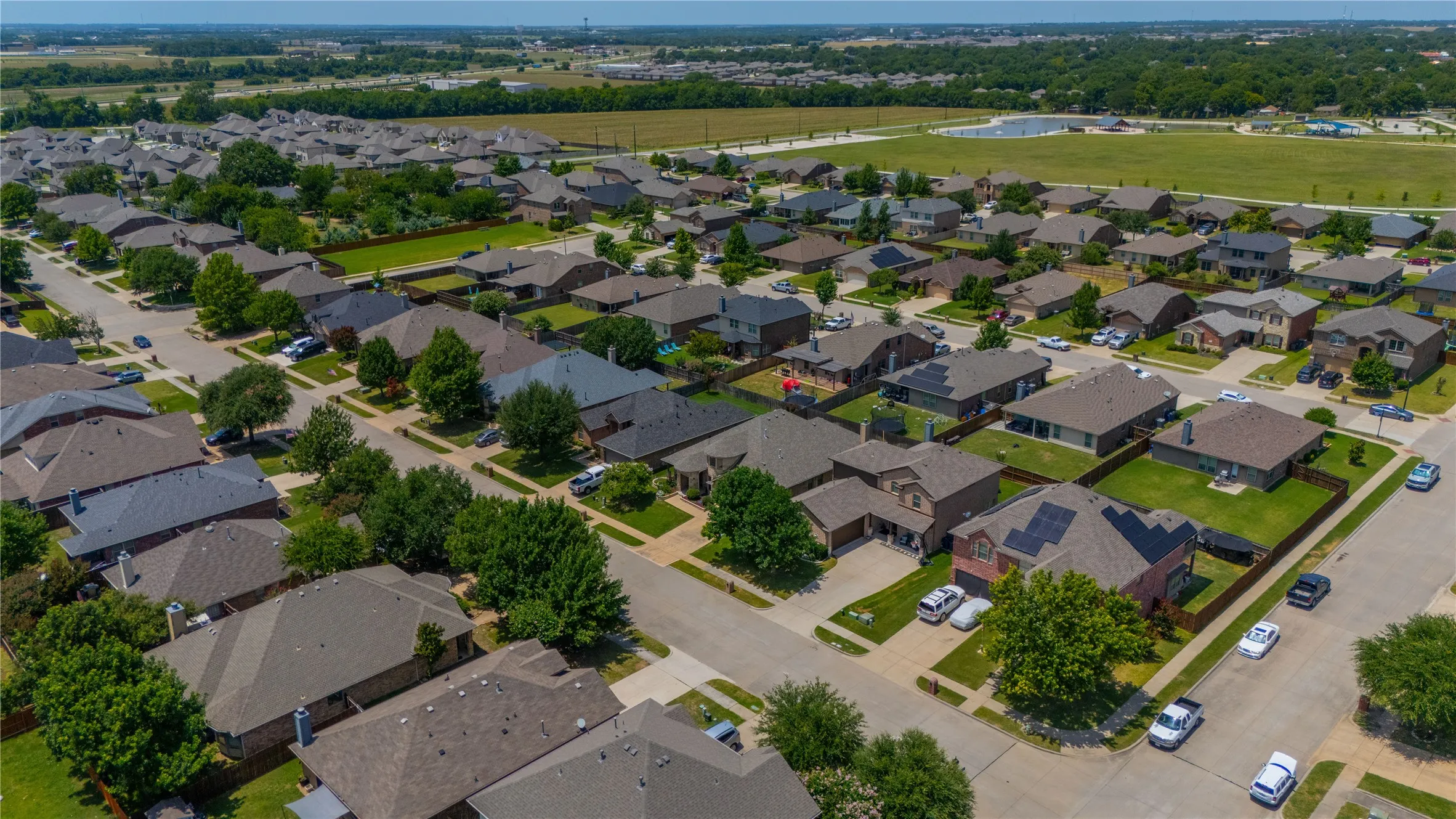 Aerial perspective showcasing a residential development with a variety of single-family homes, mature landscaping, and an expansive green space with a water feature