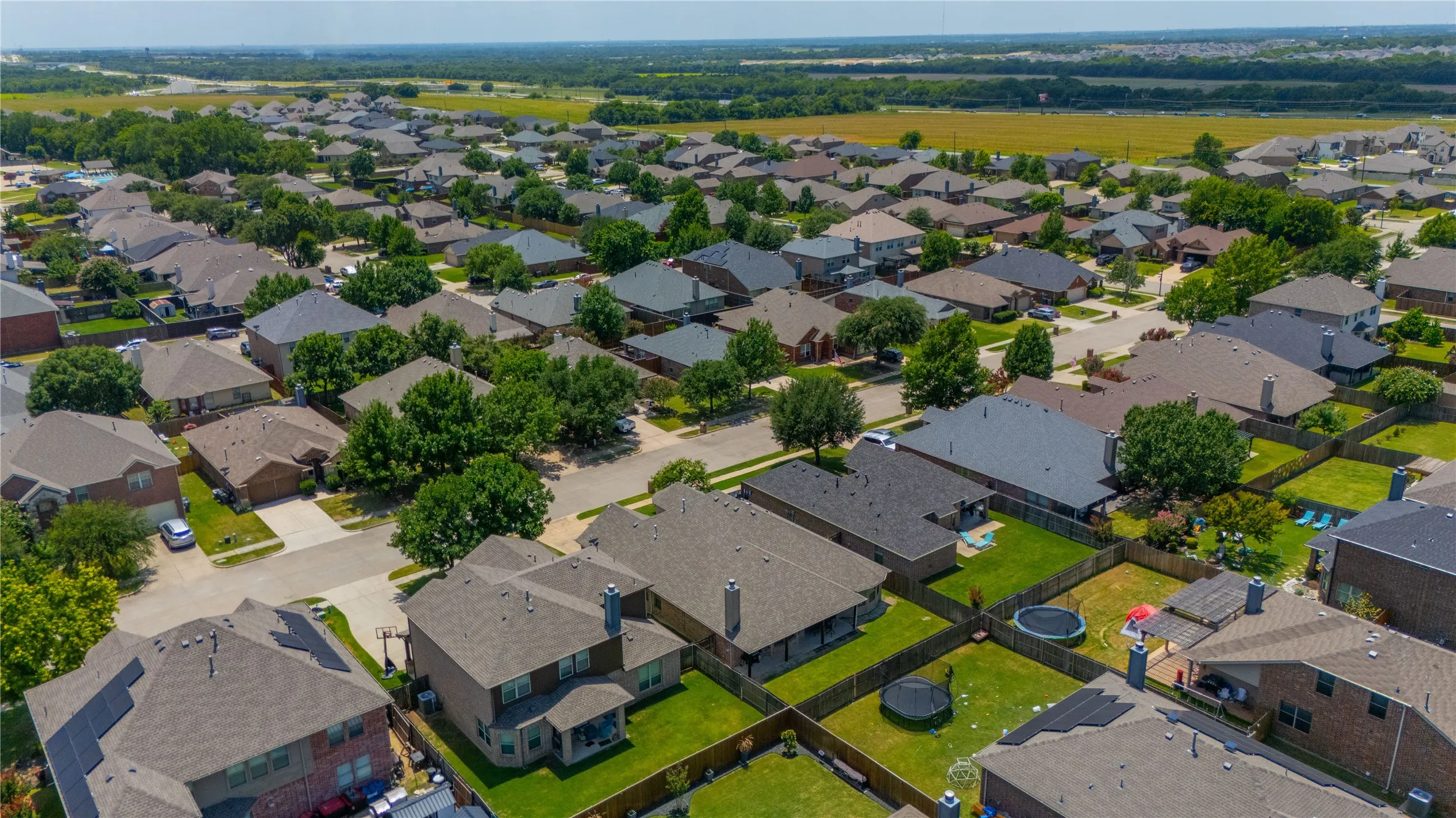 Aerial perspective showcasing a residential neighborhood with diverse roofing styles, mature trees, and individual fenced backyards