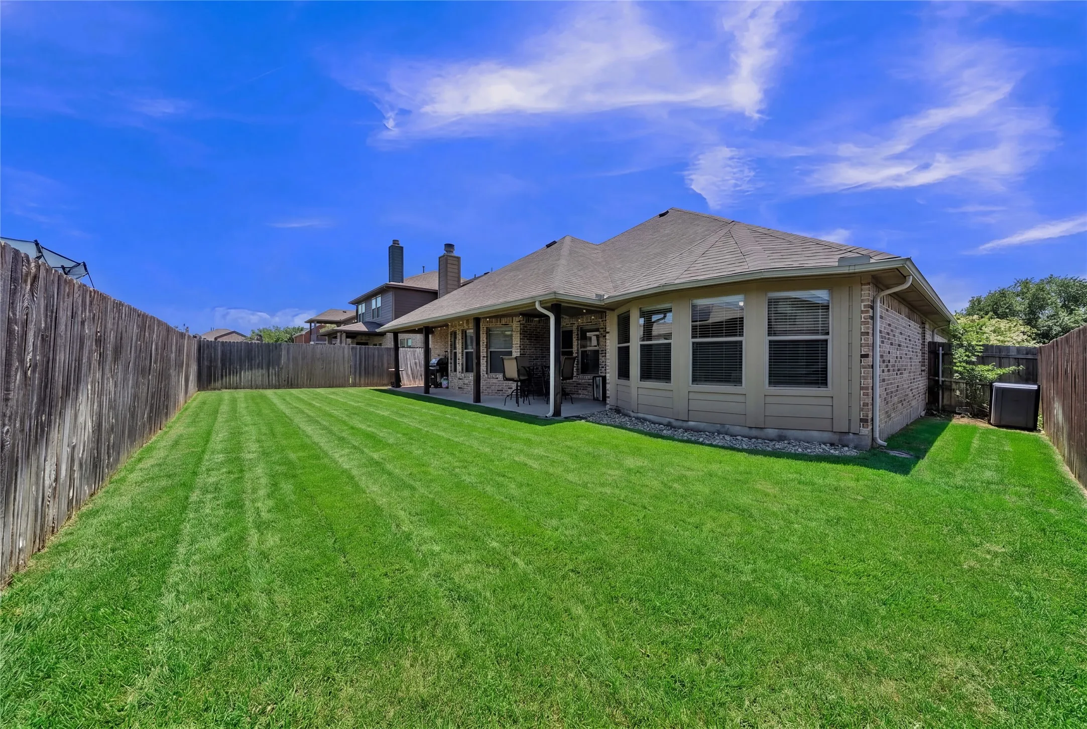 Spacious fenced backyard featuring a substantial lawn and covered patio area