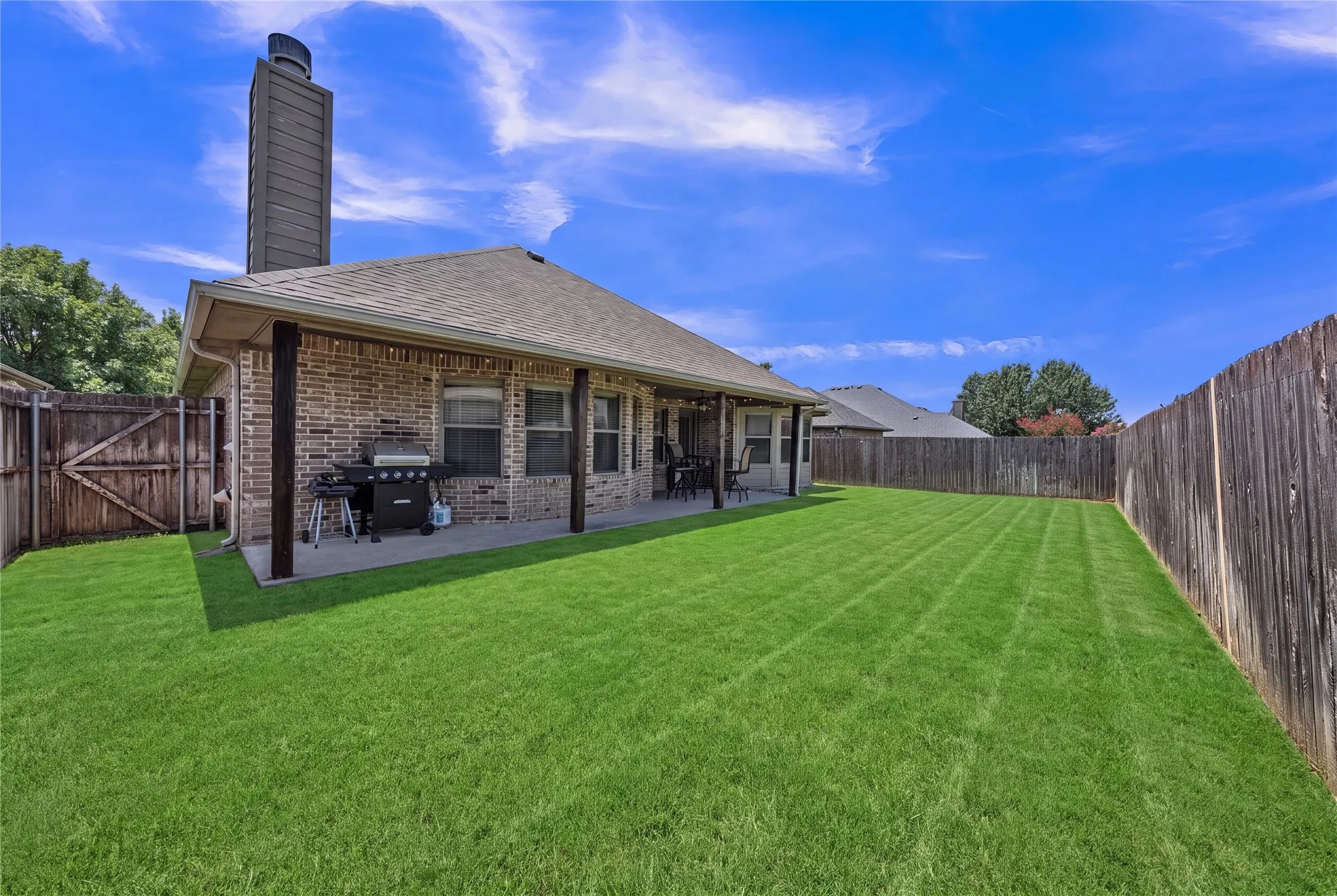 Spacious backyard featuring a substantial lawn, full privacy fencing, and a covered patio area