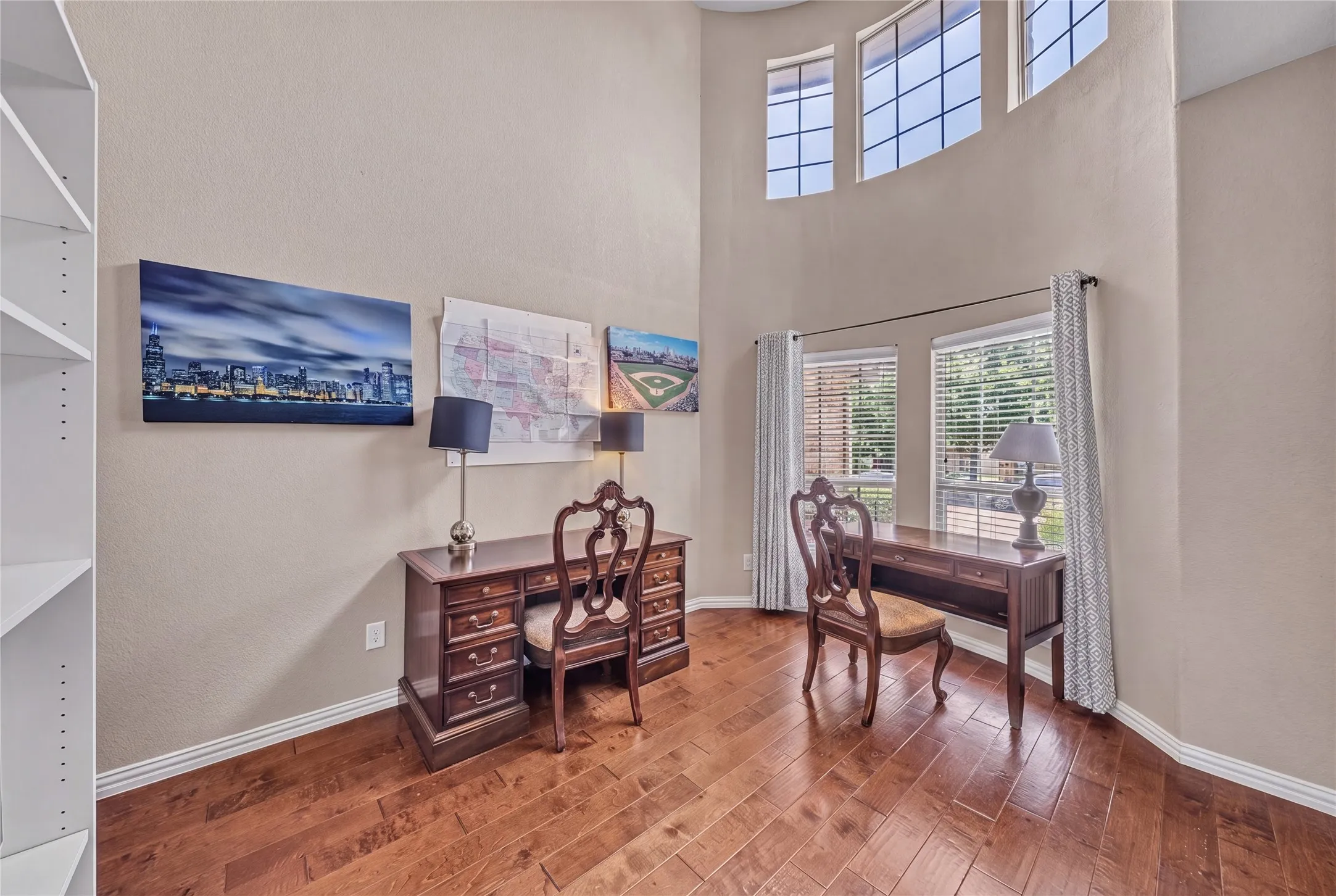 Dedicated space featuring hardwood flooring, a tall ceiling, and large windows with blinds