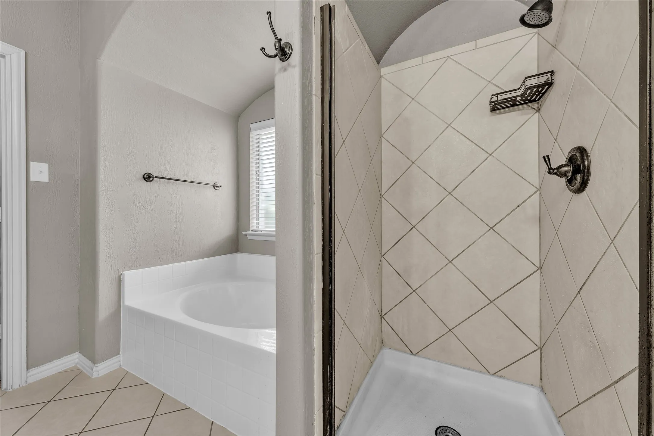 Bathroom featuring a built-in soaking tub under an arched alcove with a window, and a separate shower enclosure with diamond-patterned tiled walls and dark bronze fixtures