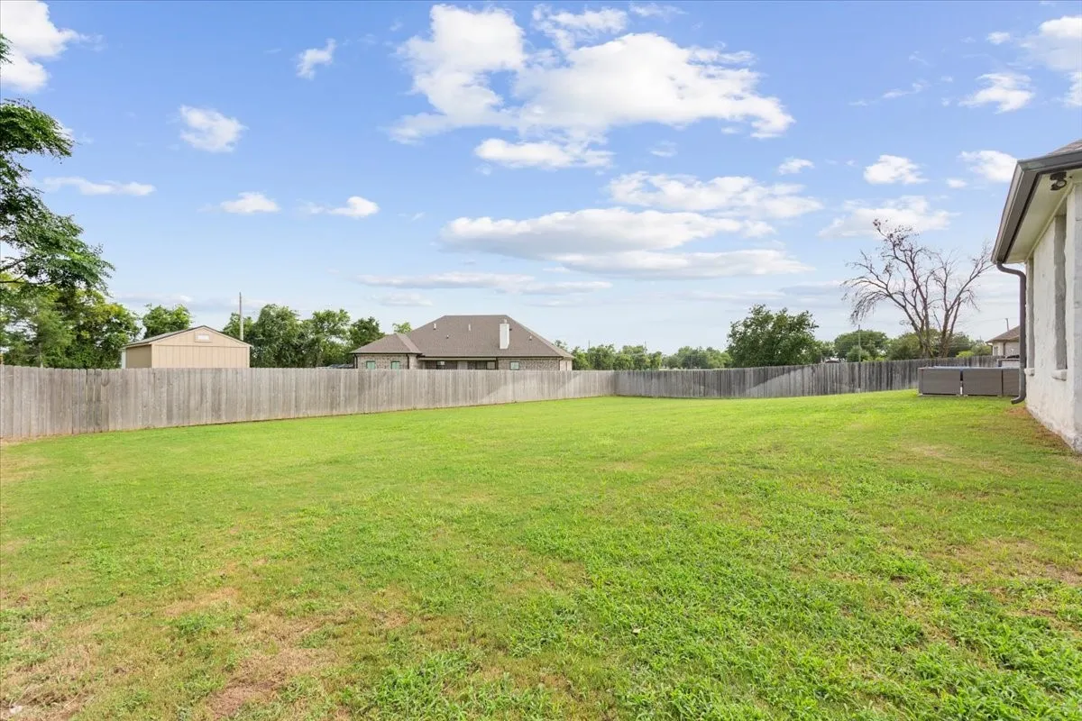 Expansive backyard featuring a large green lawn, wood privacy fencing, and a white exterior wall