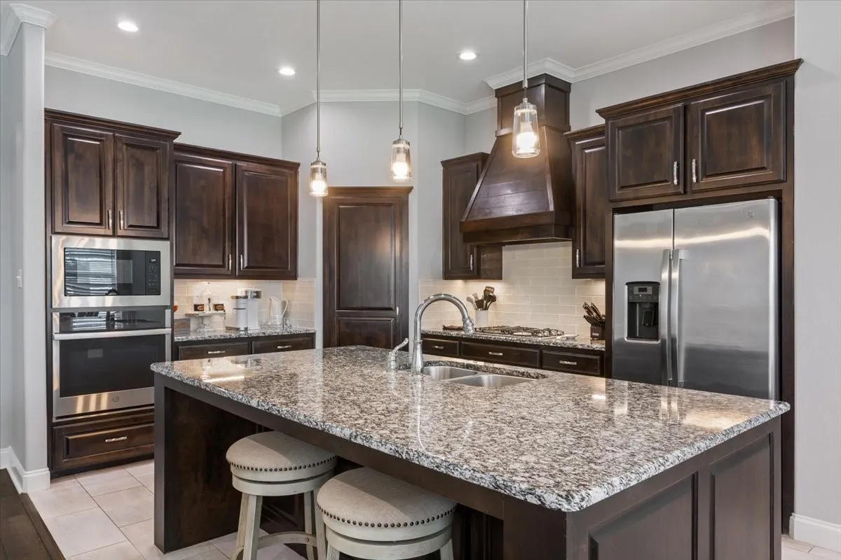 Spacious kitchen featuring dark wood cabinetry, stainless steel appliances, a large island with granite countertops, and recessed lighting