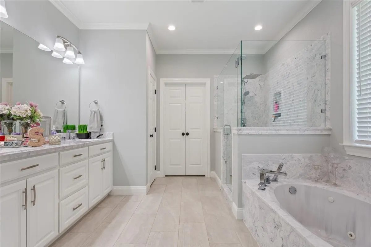 Spacious bathroom featuring a double vanity with white cabinetry and light-toned countertops, a glass-enclosed shower with tiled walls, a separate soaking tub with coordinating tile surround, and wood-finish flooring