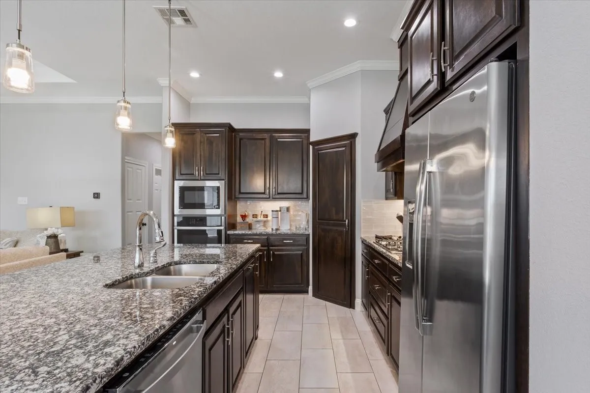Kitchen featuring a large island with a double basin stainless steel sink, granite countertops, and dark wood-finish cabinetry