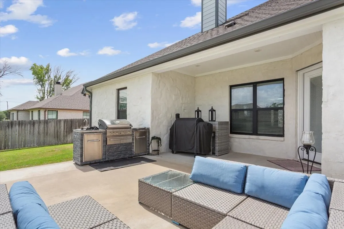 Covered patio featuring an outdoor kitchen with built-in grill and sink, stucco exterior, black-framed windows, and an exterior door with glass paneling