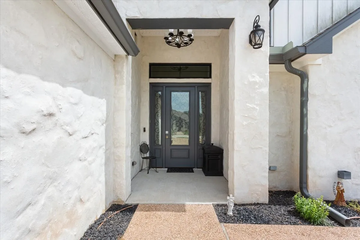 Inviting entryway featuring a dark gray double door with decorative glass inserts, framed by textured white stucco
