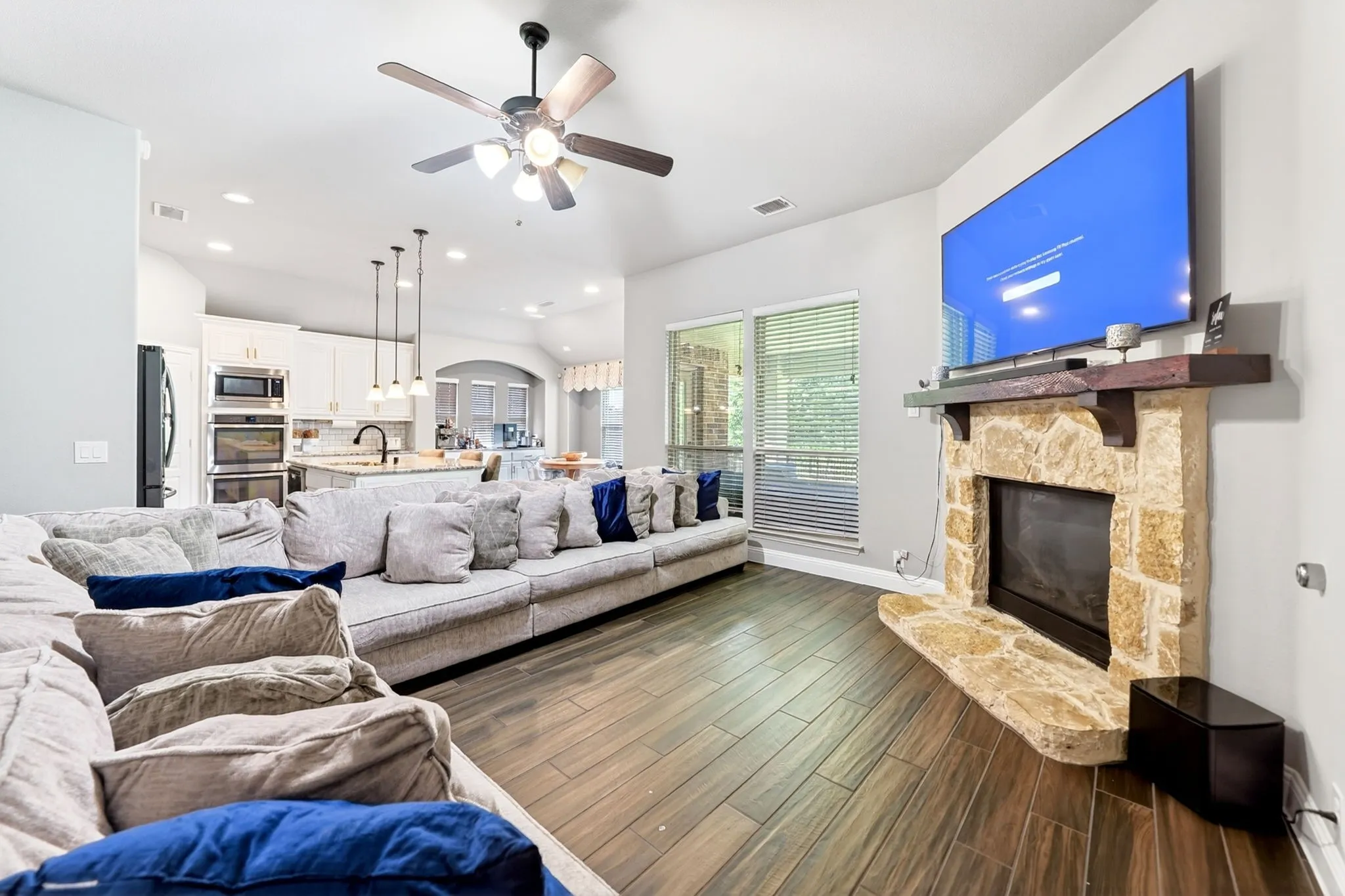 Living area featuring a stone fireplace with a wood mantle, wood-finish flooring, and a ceiling fan