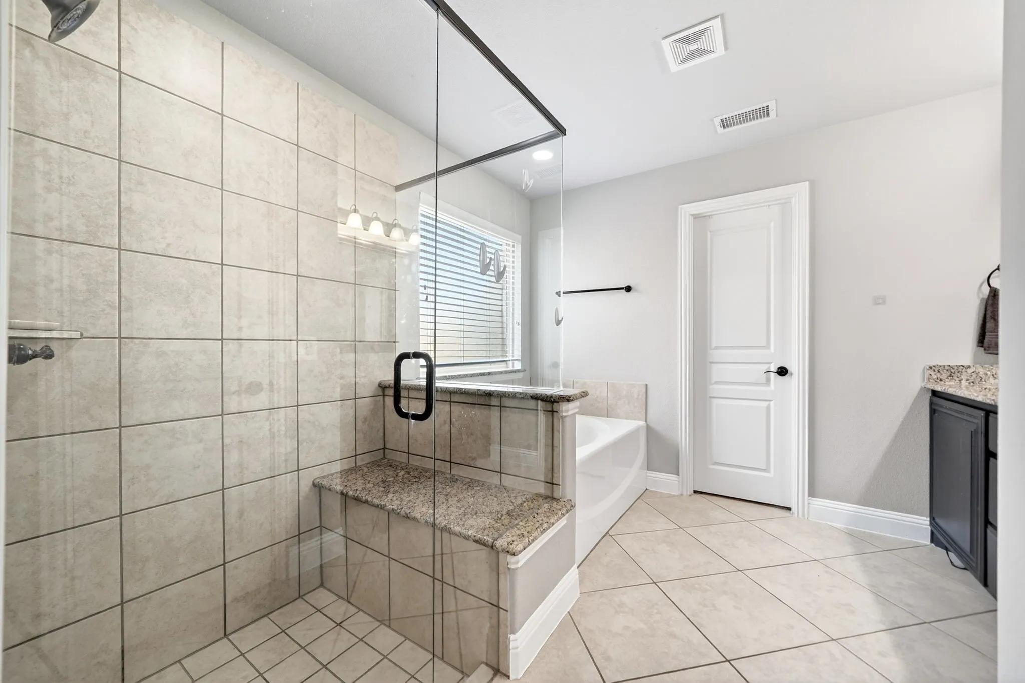 Tiled shower enclosure featuring a glass door, built-in granite bench, and overhead shower fixture