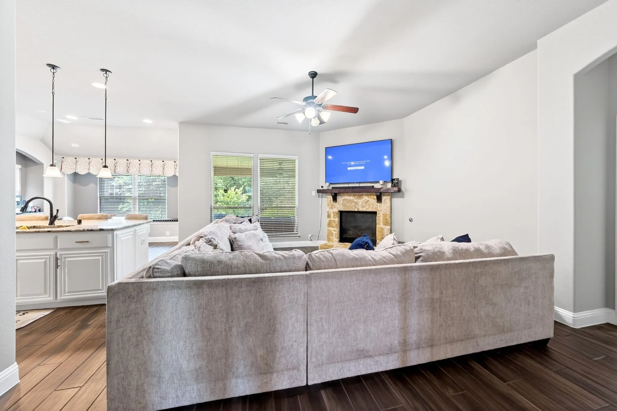 Spacious interior featuring wood-finish flooring, a stone fireplace with a wood mantle, and a ceiling fan