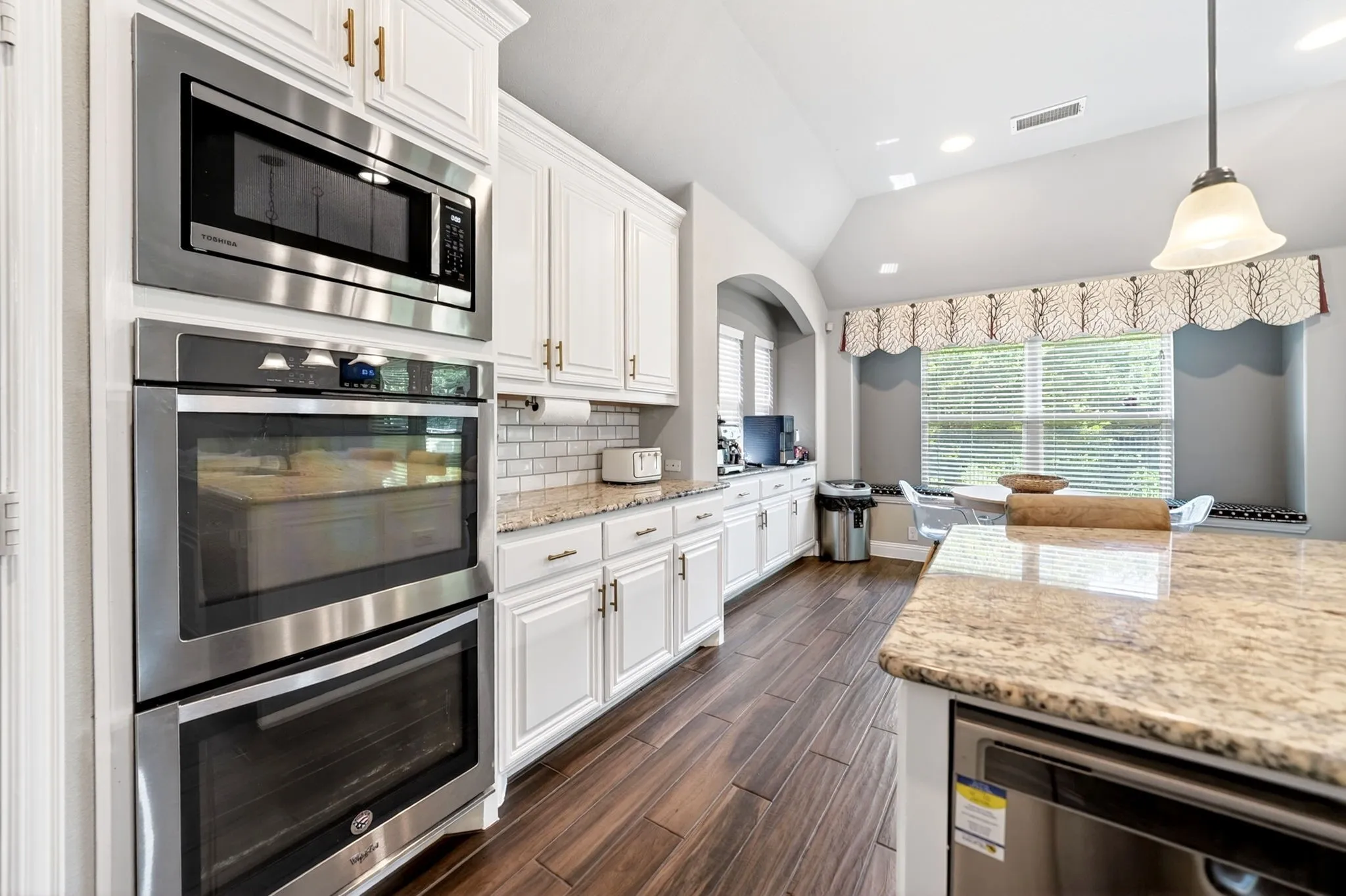White cabinetry with gold-tone hardware, stainless steel built-in microwave, and double ovens