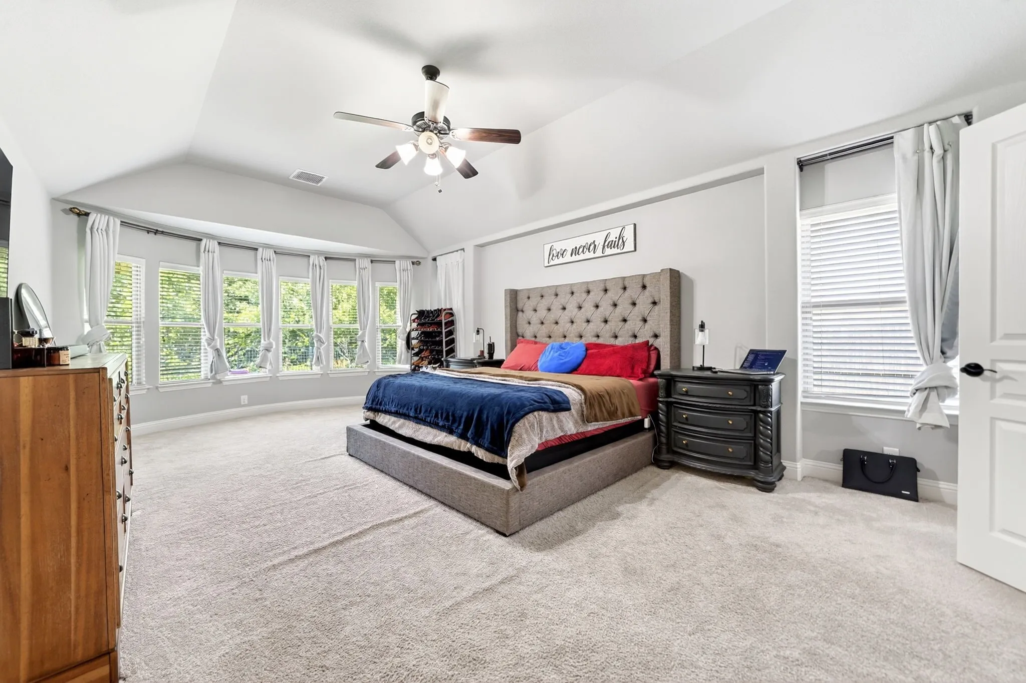 Spacious room featuring a vaulted ceiling with a ceiling fan, a bay window with multiple panels, and light-colored carpet flooring