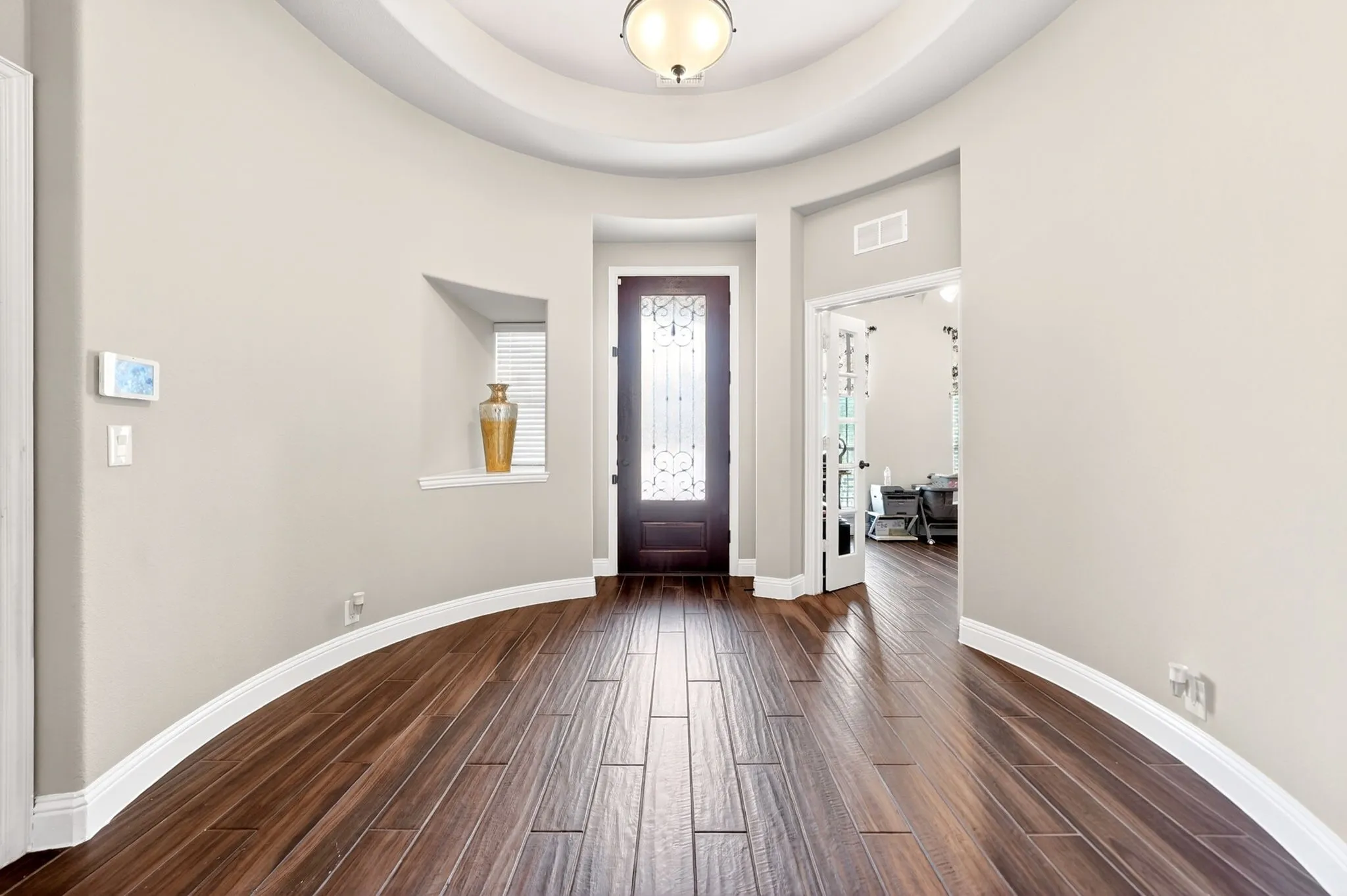Foyer with wood-finish flooring, a tray ceiling, and a dark wood entry door with decorative glass