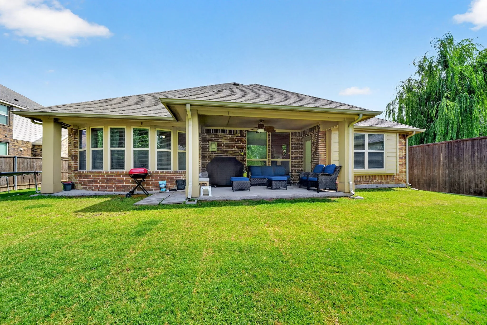 Expansive backyard featuring a covered patio, brick and siding exterior, multiple windows, and a mature tree