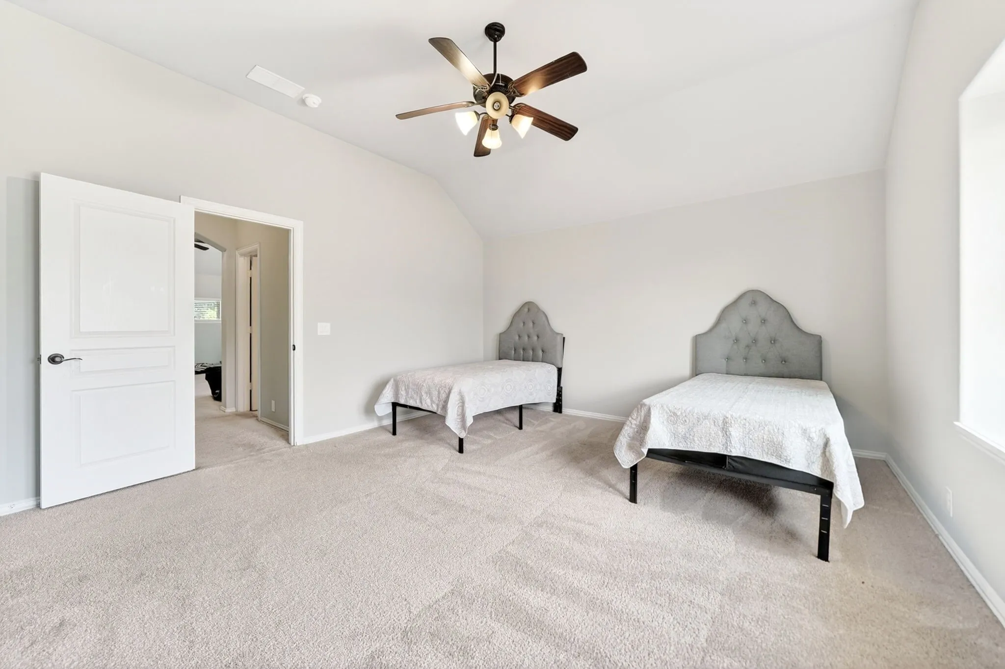 Spacious room featuring vaulted ceilings, light-colored carpet flooring, and a ceiling fan with integrated lighting