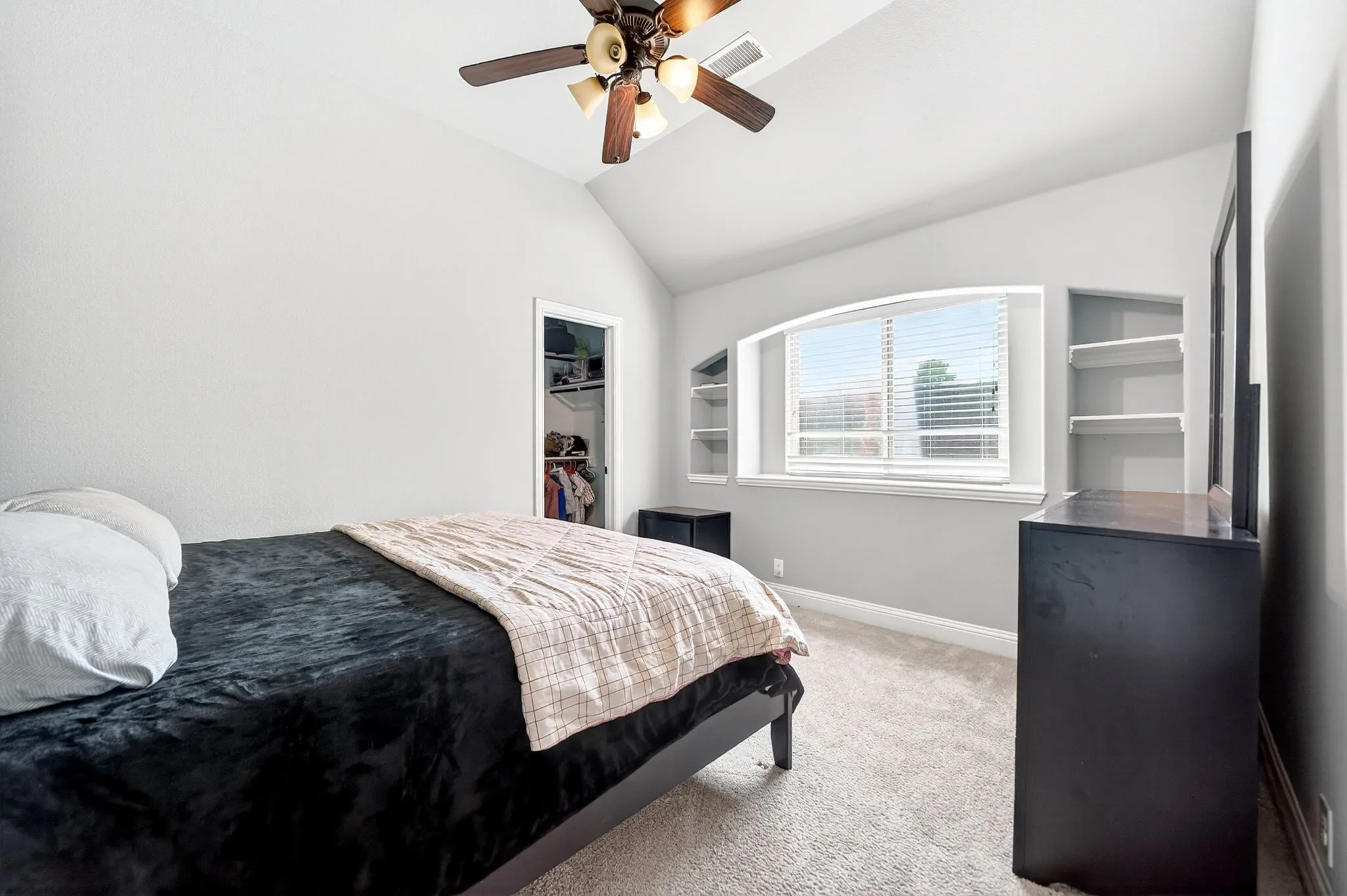 Vaulted ceiling room featuring a ceiling fan with integrated lighting, a window with blinds, and built-in shelving units