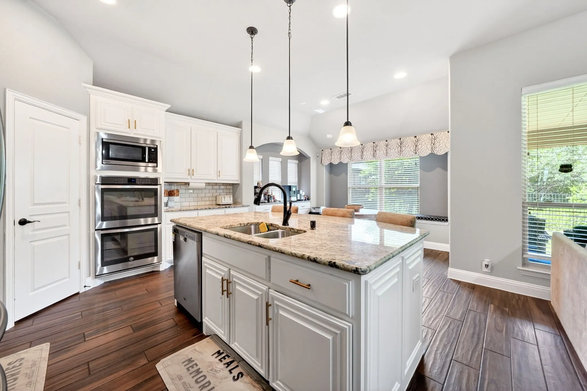Modern kitchen featuring white cabinetry, stone countertops, stainless steel appliances, wood-finish flooring, and a subway tile backsplash with mosaic accent