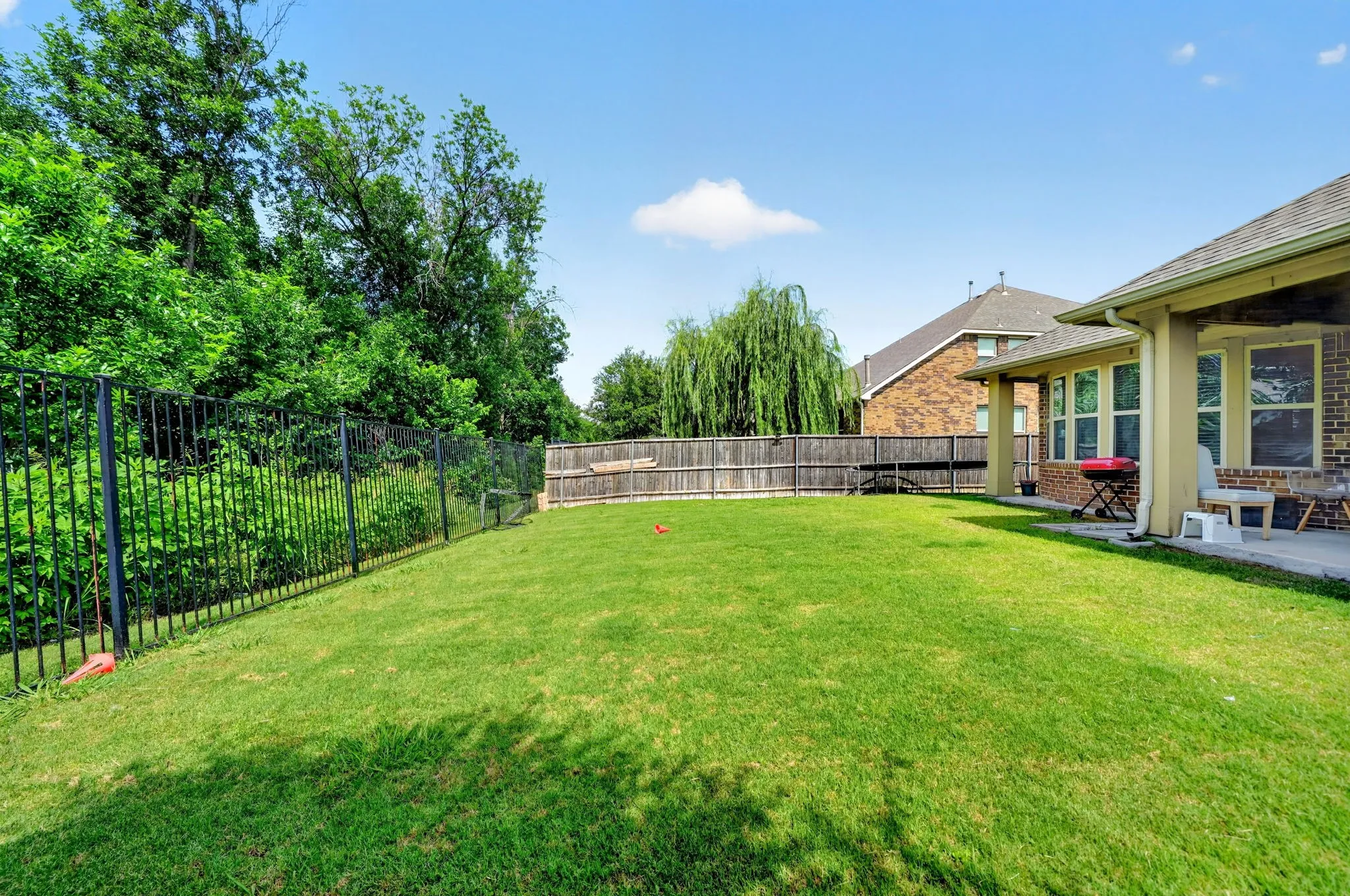 Expansive lawn area featuring a black metal fence, a wood privacy fence, and a concrete patio