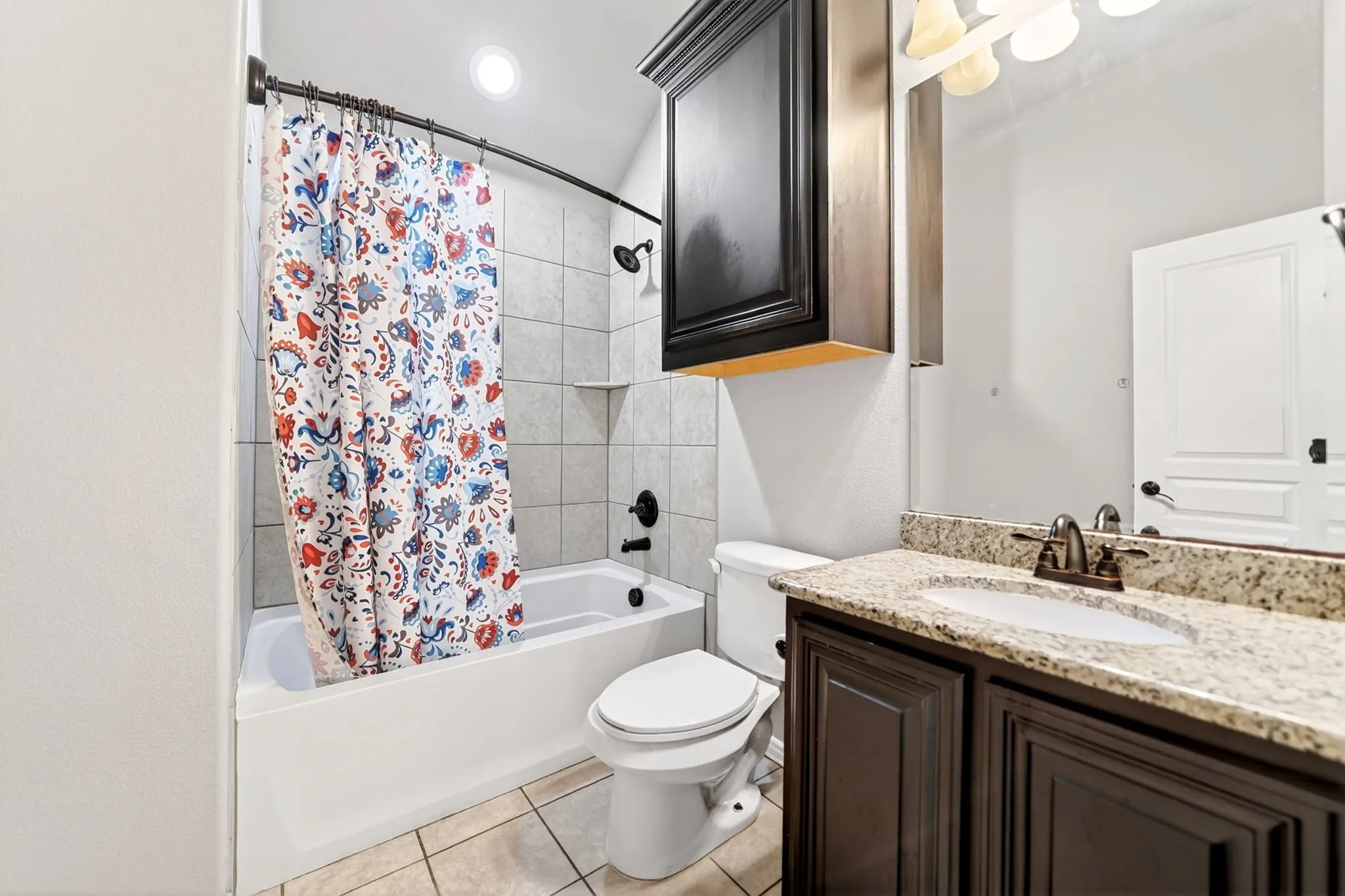 Full bathroom featuring a tub/shower combination with tile surround, a dark wood-finish vanity with a granite countertop, and tile flooring