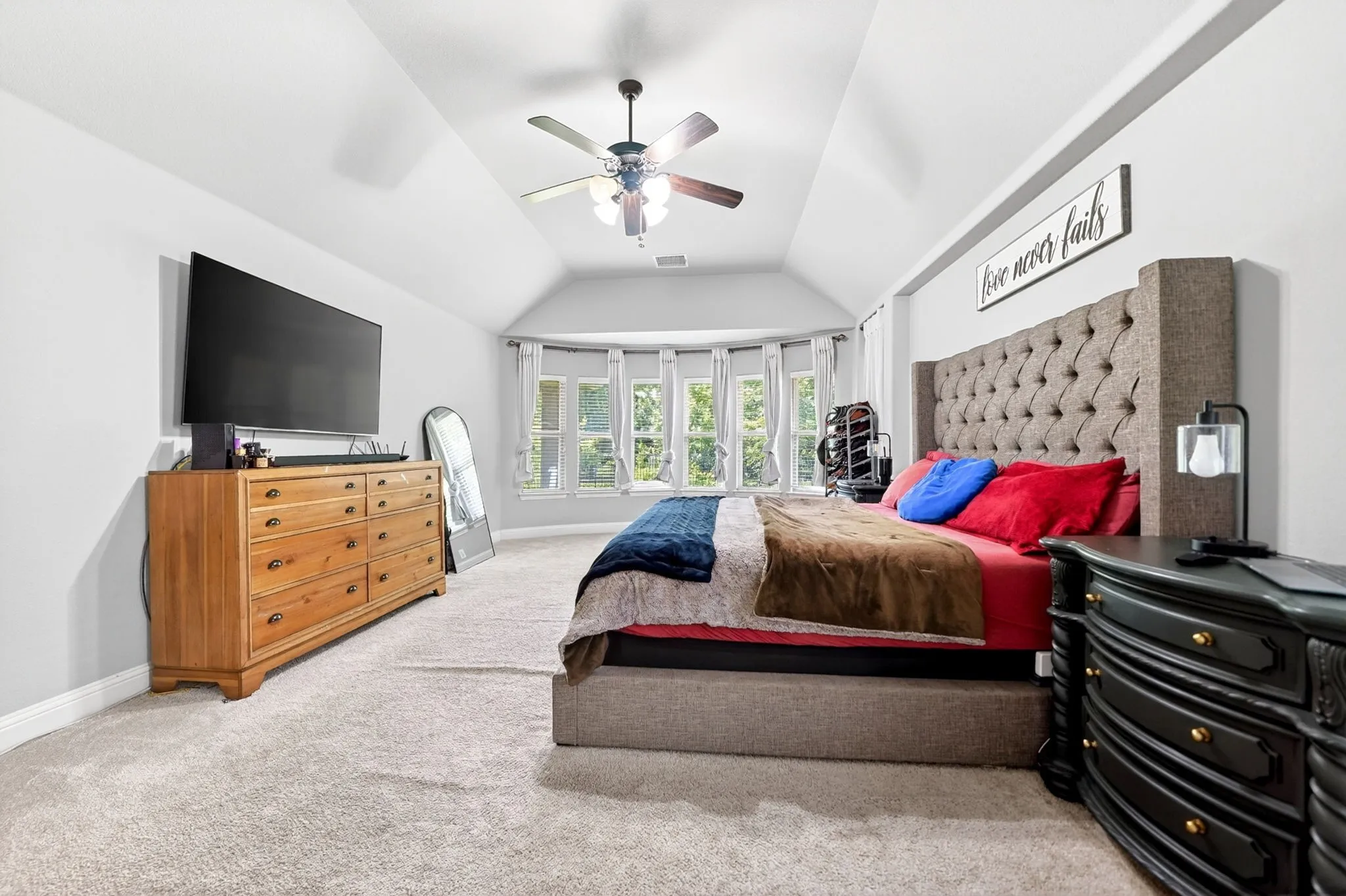 Spacious bedroom featuring light neutral carpet flooring, a vaulted ceiling, and a ceiling fan