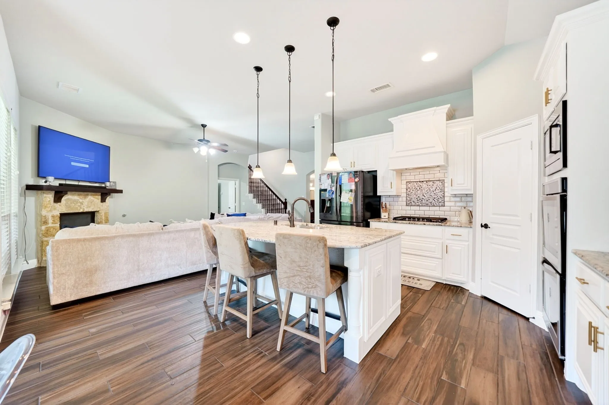 Open-concept living space featuring wood-finish flooring, a stone fireplace, and a kitchen island with pendant lighting