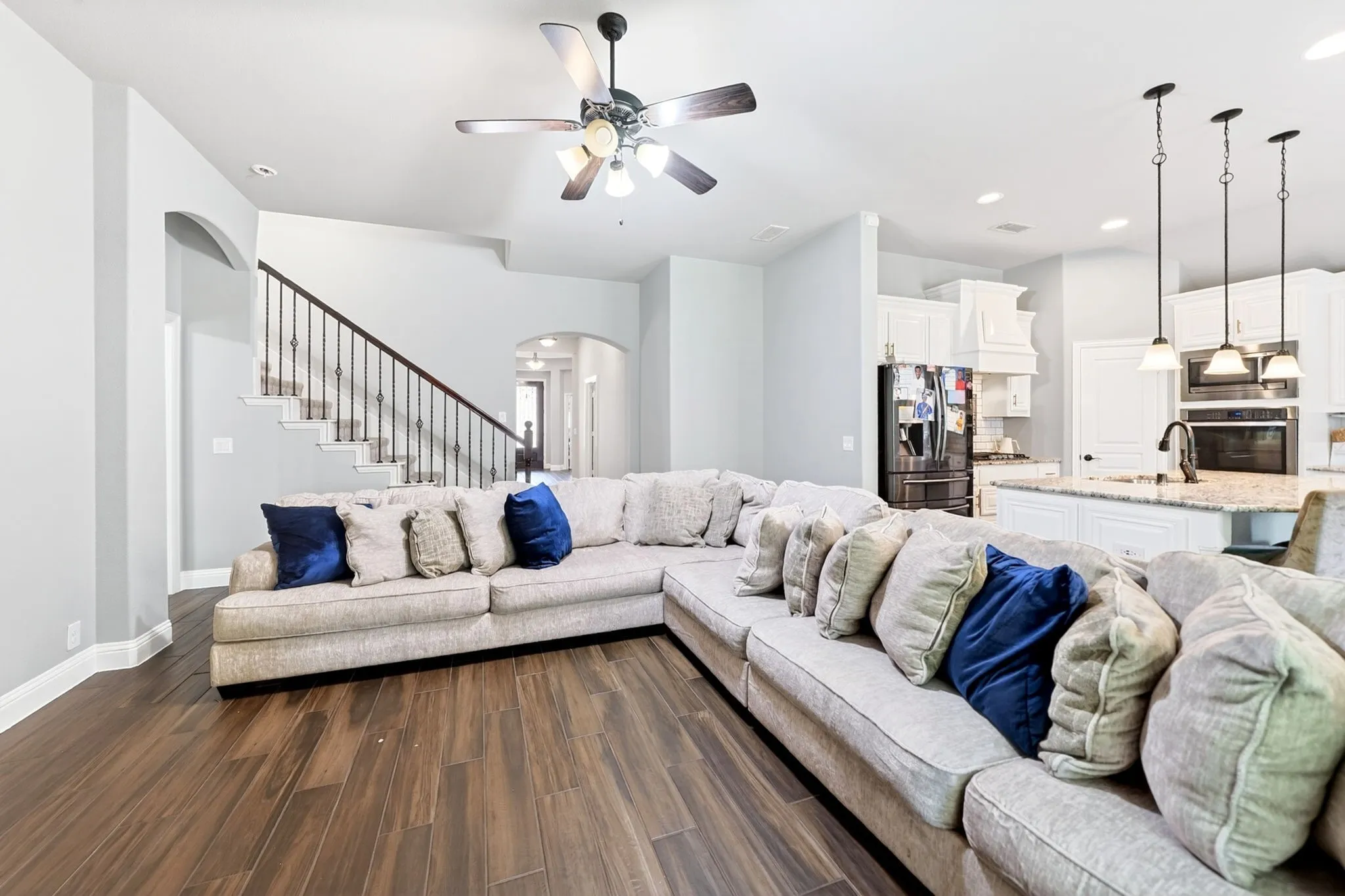 Spacious living area featuring wood-finish flooring, a ceiling fan with integrated lighting, and an open concept layout