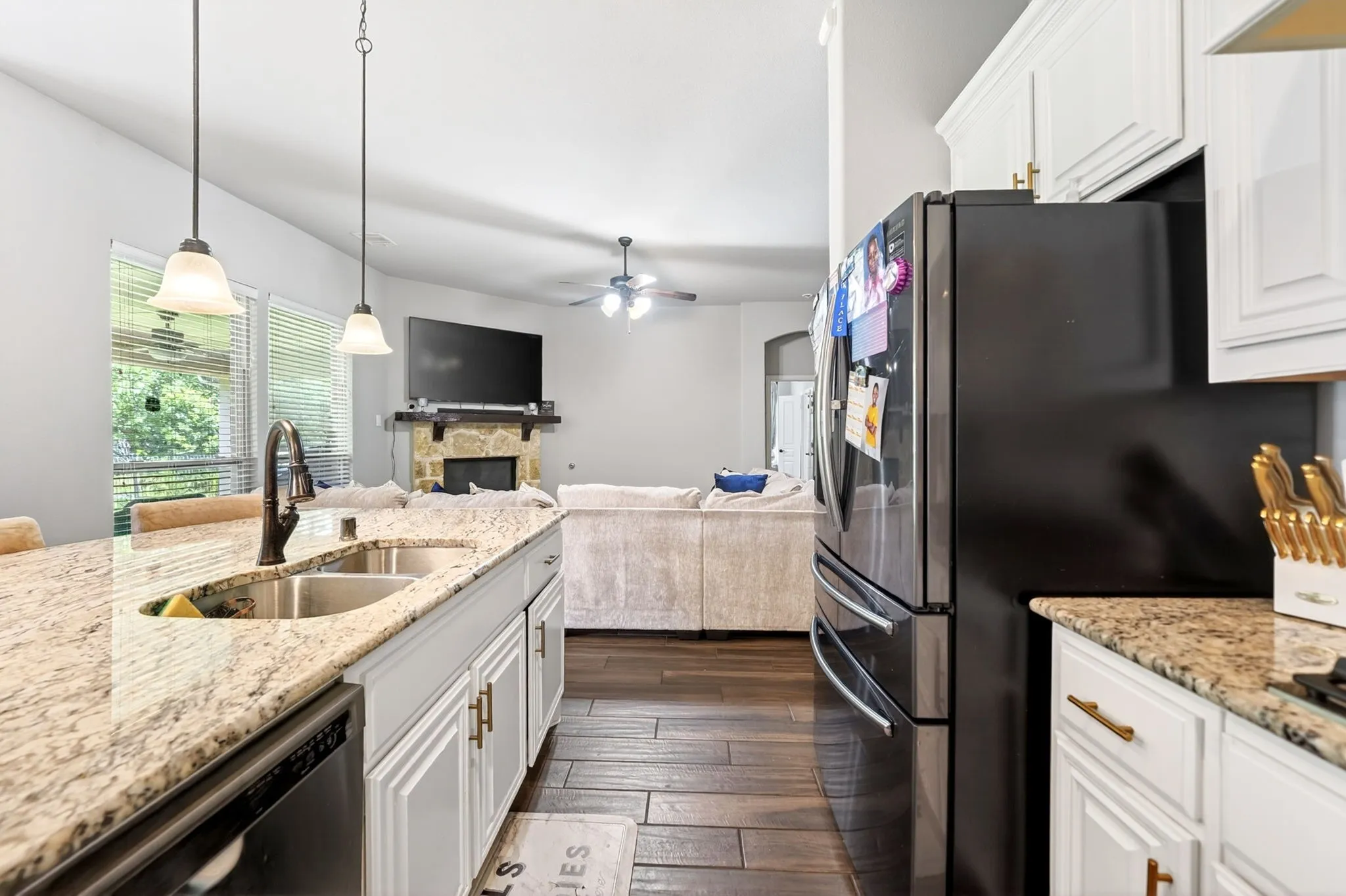 Kitchen island featuring a double basin sink with a gooseneck faucet, light granite-style countertops, and pendant lighting