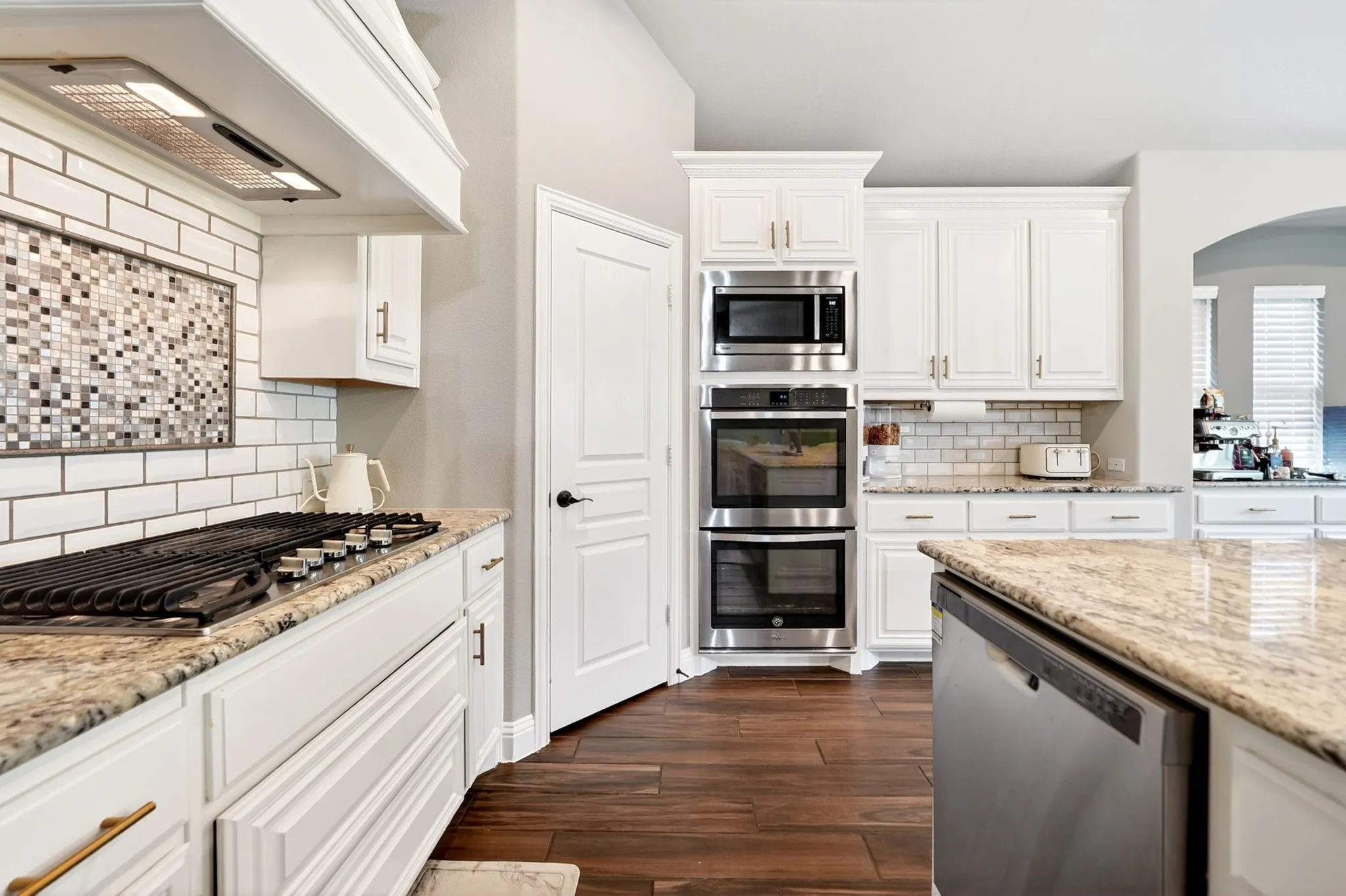 Modern kitchen featuring white cabinetry, stone countertops, stainless steel appliances, wood-finish flooring, and a subway tile backsplash with mosaic accent