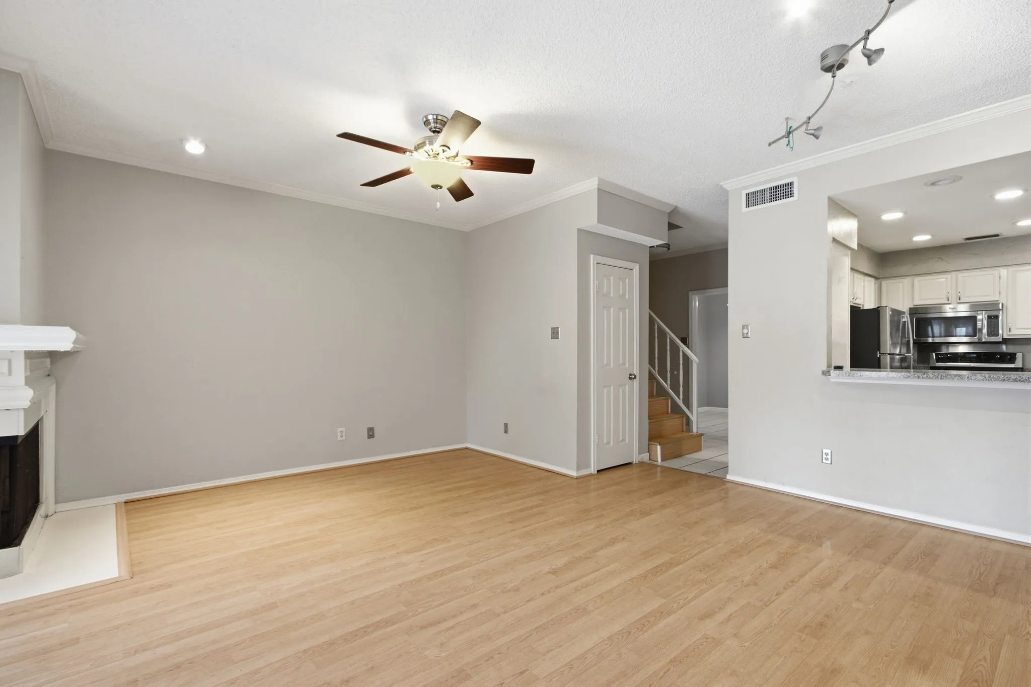 Spacious living area featuring wood-finish flooring, a decorative fireplace with a white mantel, and crown molding