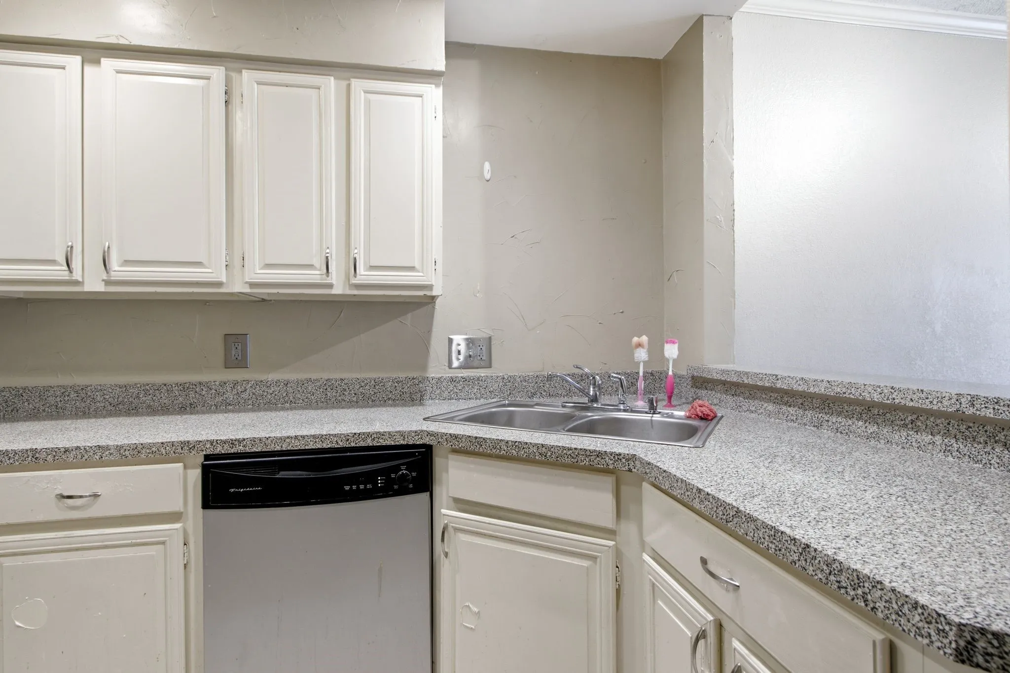 Kitchen featuring white cabinetry, speckled countertops, a stainless steel double basin sink, and an integrated dishwasher