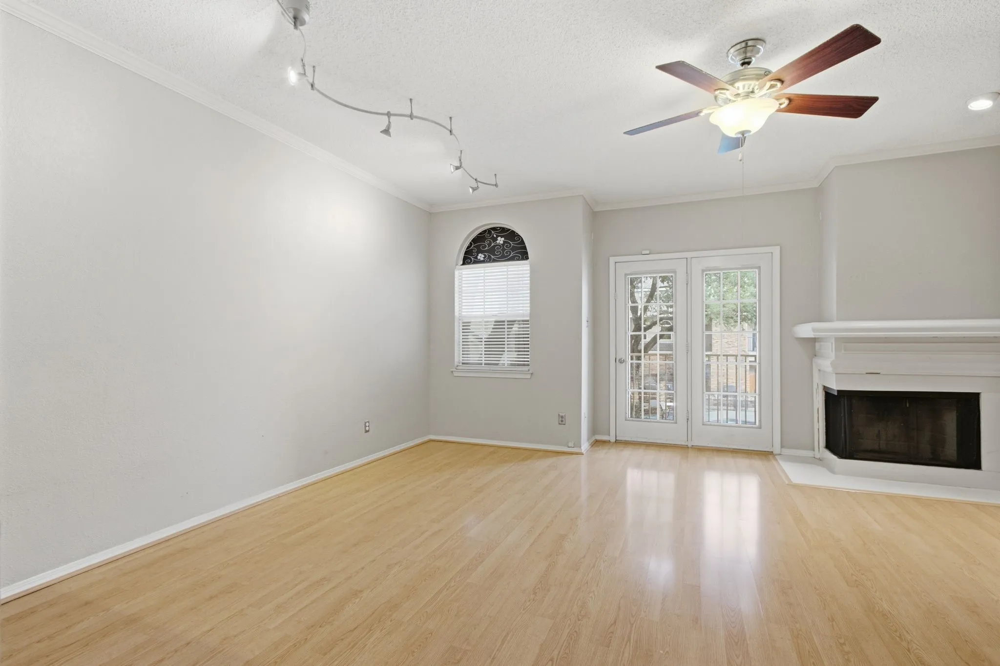Bright living space featuring wood-finish flooring, a white mantel fireplace, a decorative arched window with blinds, and French doors