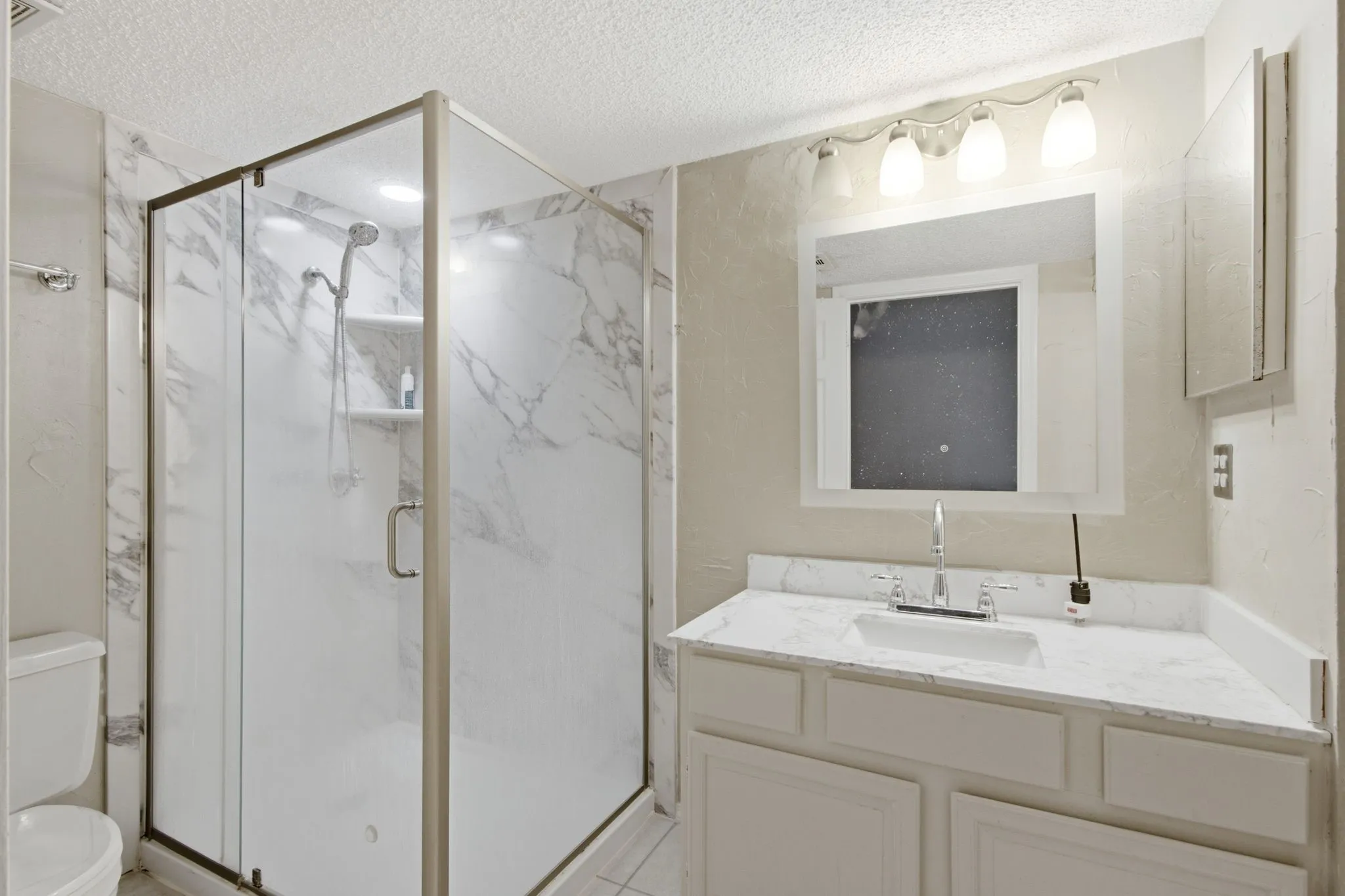 Glass-enclosed shower with white marble-look paneling, integrated shelving, and a rain showerhead