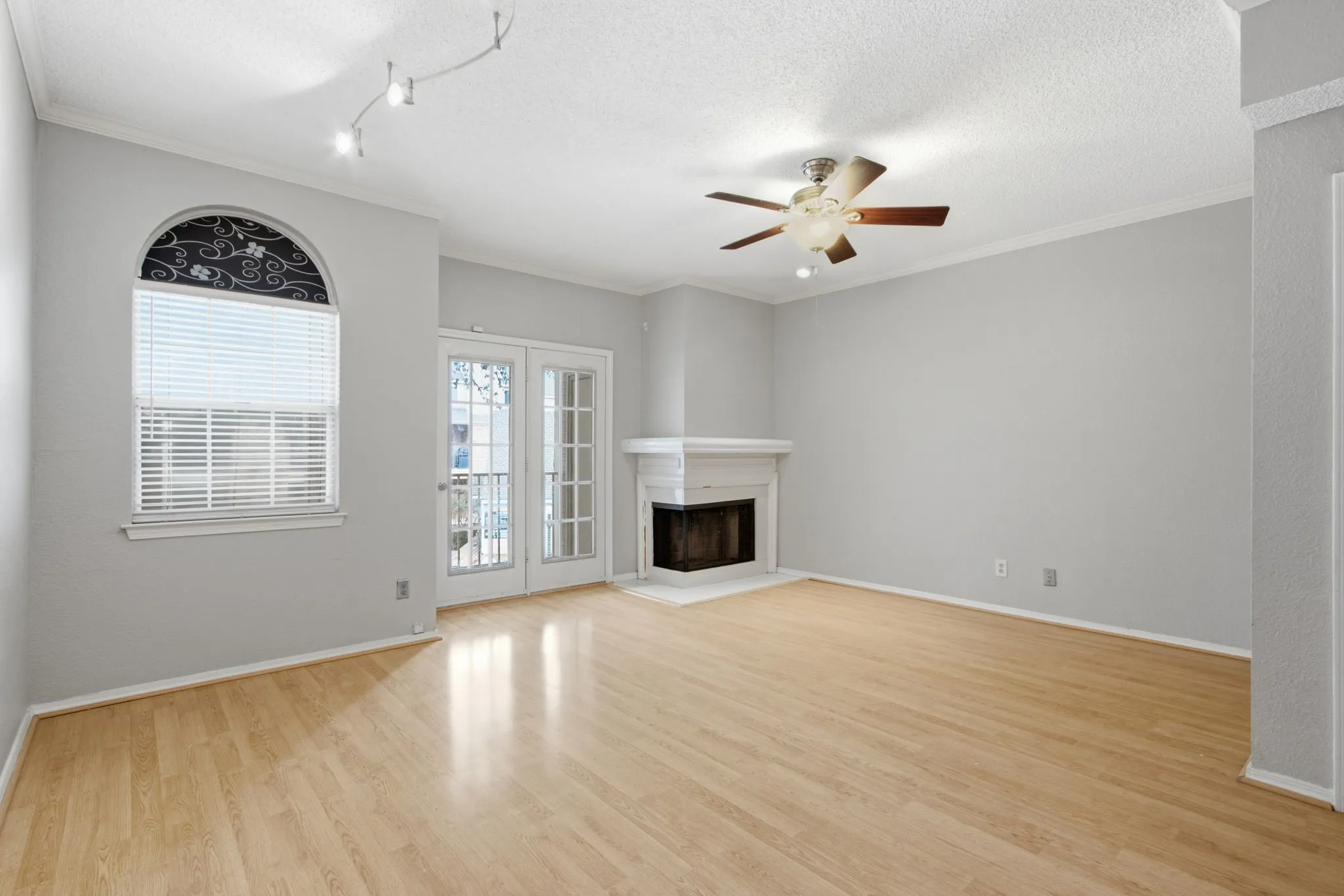 Spacious room featuring wood-finish flooring, a white mantel fireplace, and double French doors