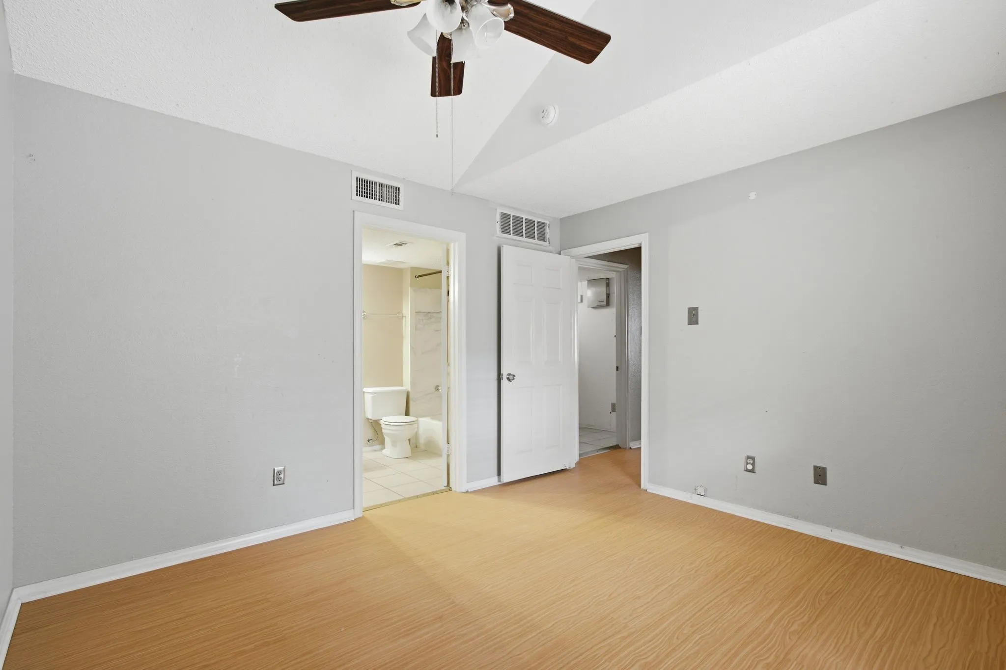 Spacious room featuring light wood-finish flooring, light gray wall paint, and a vaulted ceiling with a ceiling fan