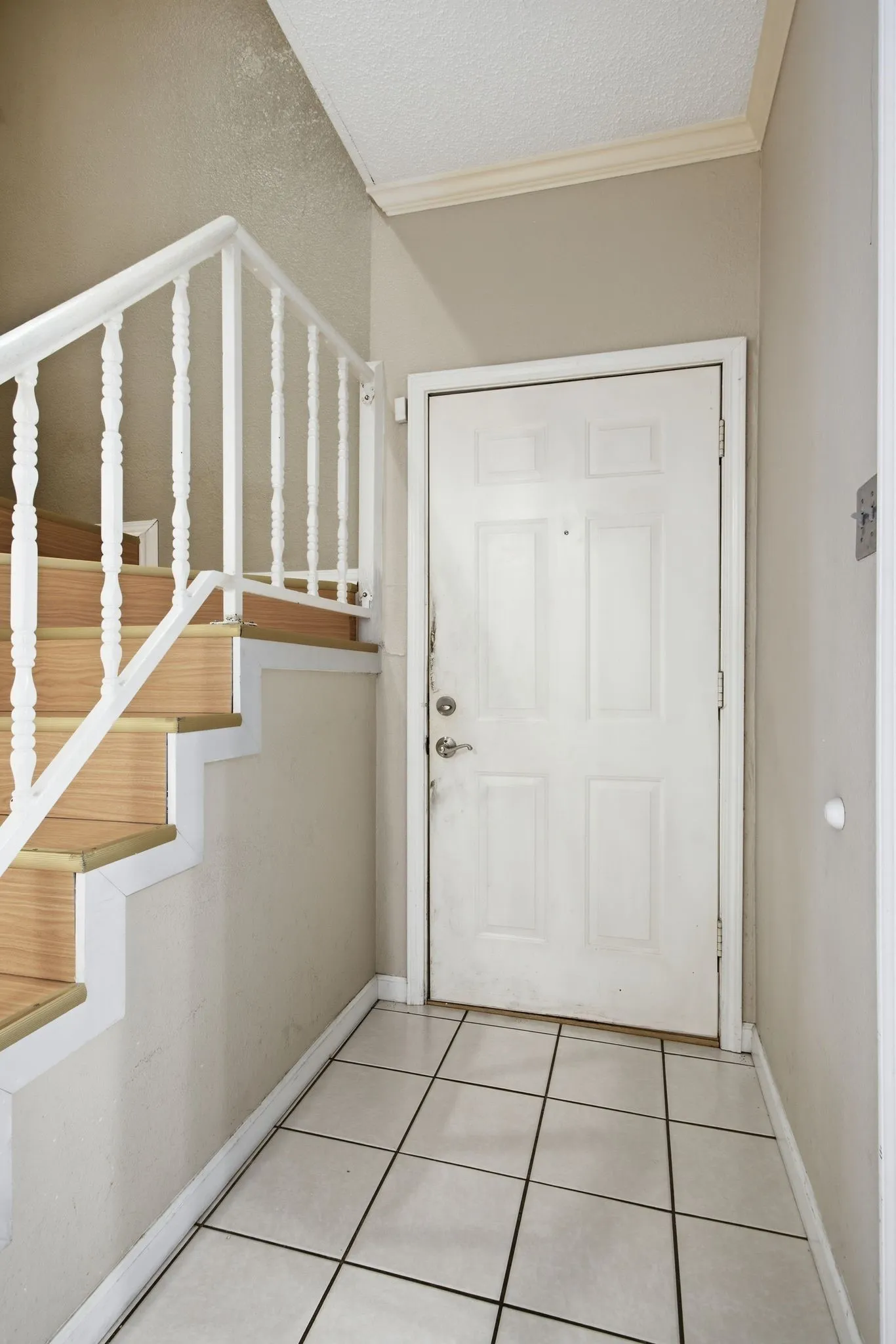 Foyer featuring light-toned tile flooring, a paneled entry door, and a staircase with wood-finish treads and white balusters