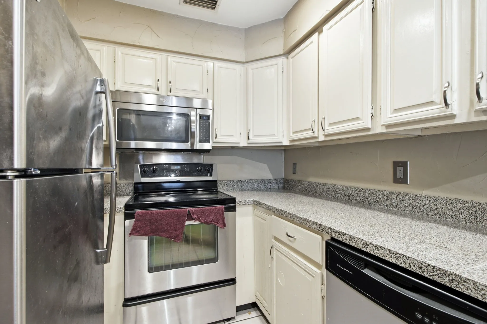 Kitchen featuring white cabinetry, stainless steel appliances, speckled countertops, and a built-in dishwasher