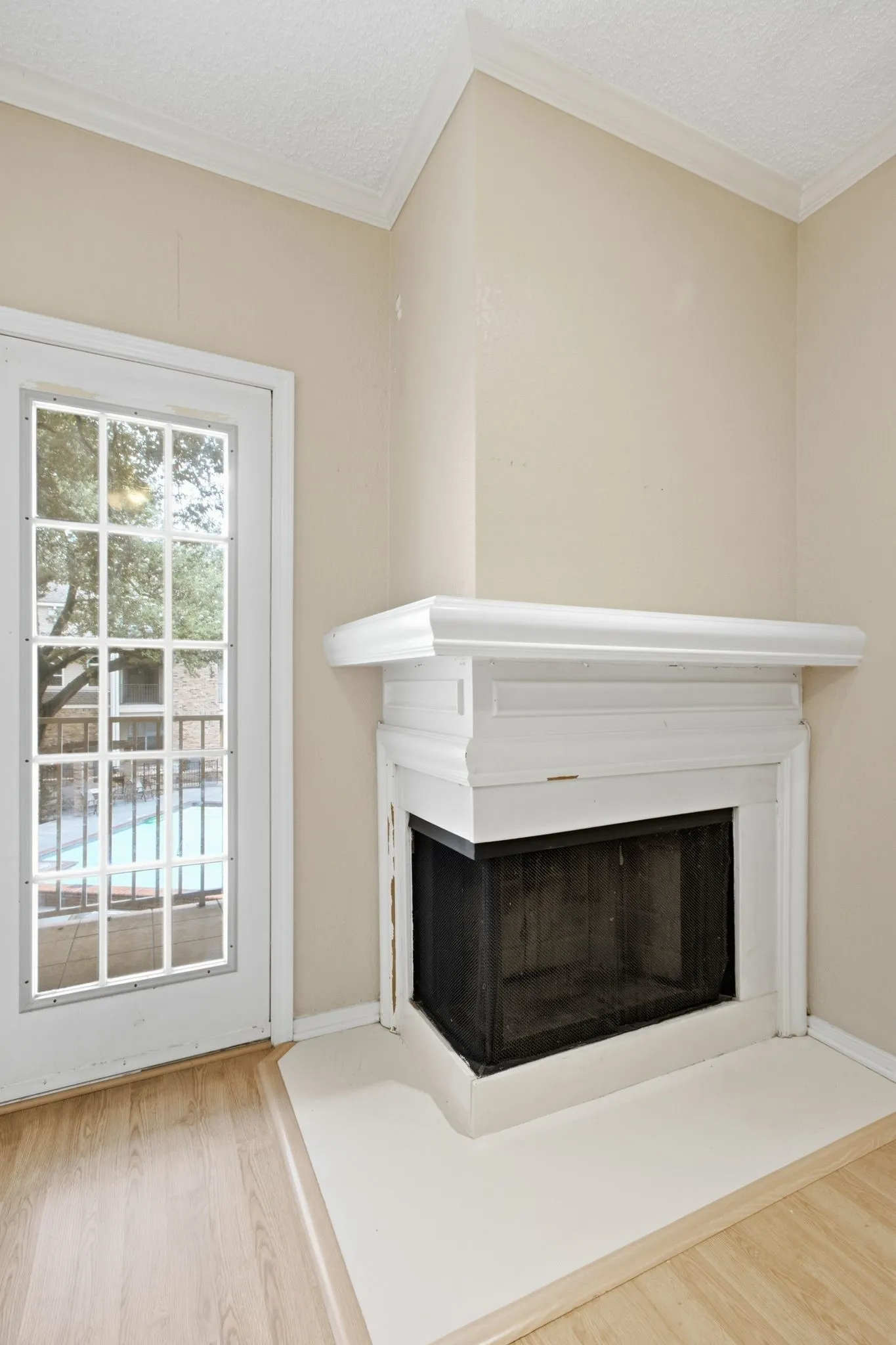 Corner fireplace with a white mantel and hearth, set against light neutral walls and wood-finish flooring