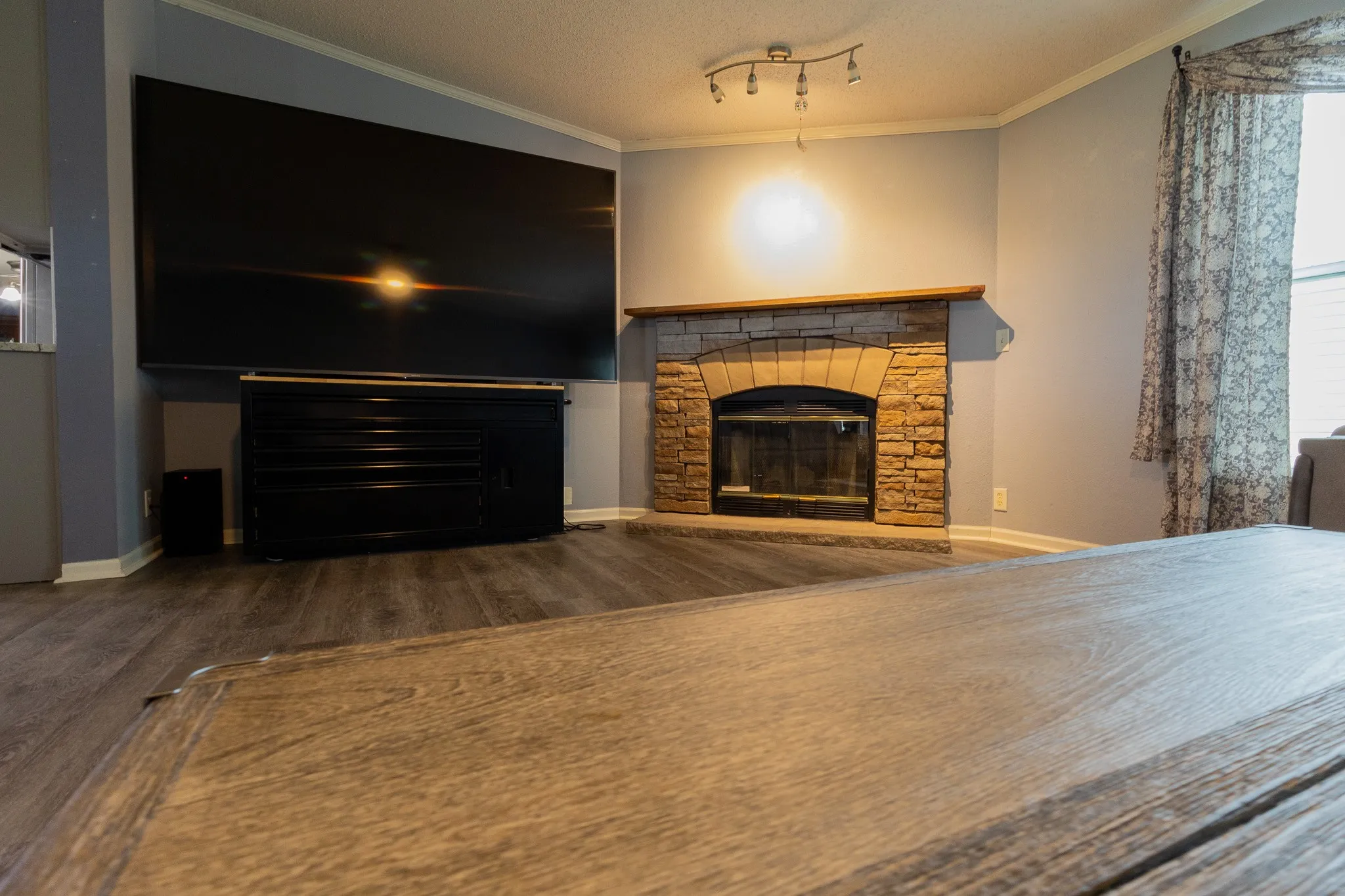 Living area featuring a stone-clad fireplace with a wood mantel, wood-finish flooring, and crown molding