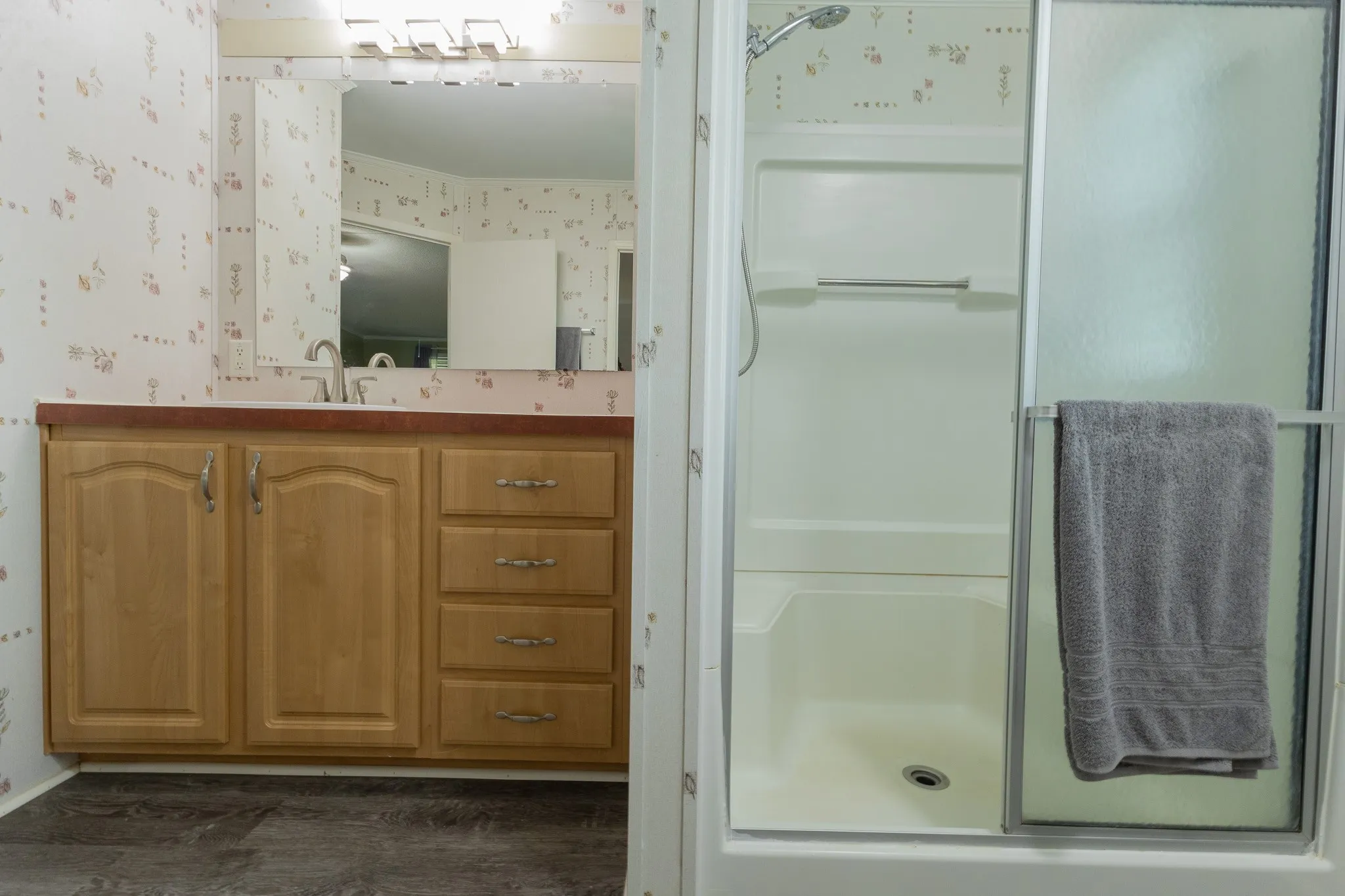 Bathroom featuring a light wood-finish vanity with a pink-hued countertop, undermount sink, and a mirrored wall