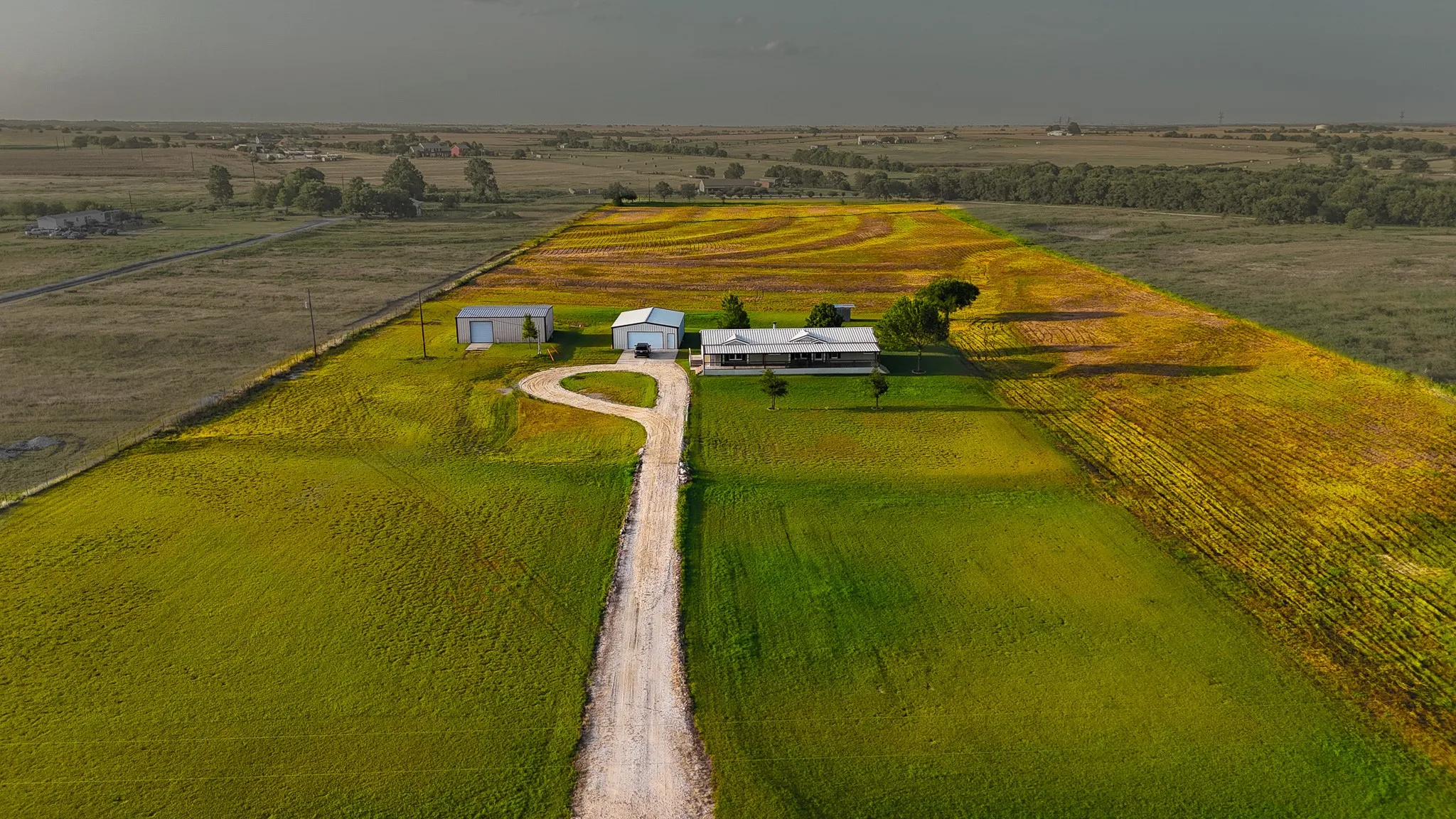 Expansive rural property featuring a long gravel driveway, a single-story residence with a covered porch, and two detached outbuildings