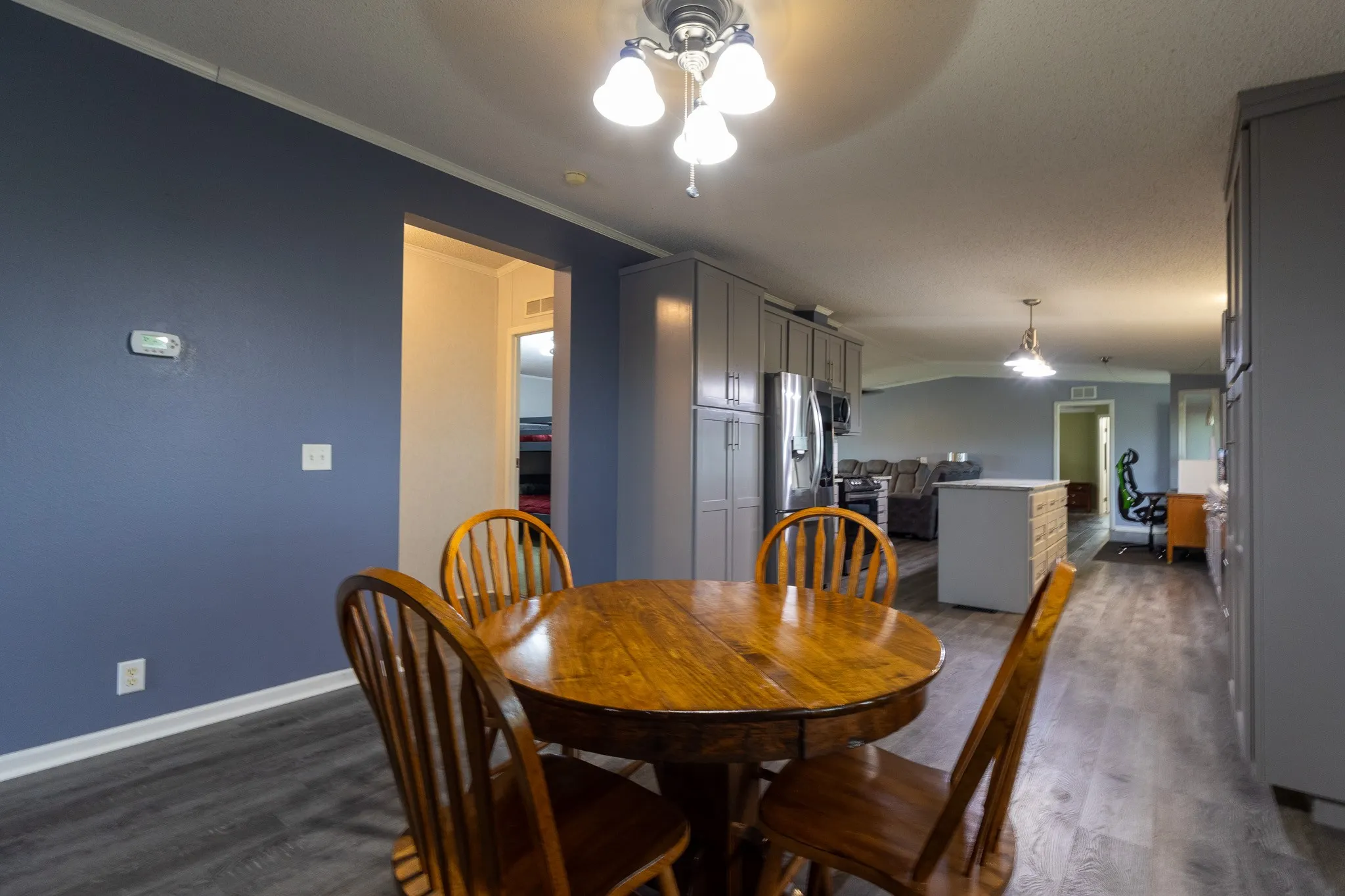 Open-concept interior featuring wood-finish flooring, a ceiling-mounted light fixture, and a spacious kitchen area with grey cabinetry and stainless steel appliances