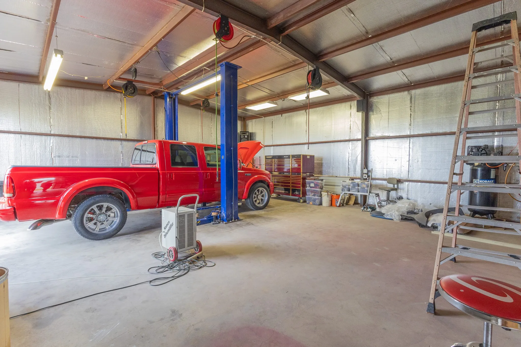 Spacious workshop featuring a durable concrete floor, exposed metal beam construction, and insulated walls