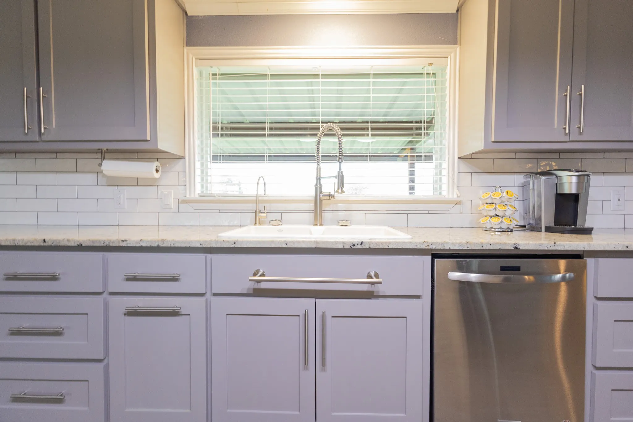 Kitchen featuring light gray cabinetry with brushed nickel hardware, a white subway tile backsplash, and speckled countertops