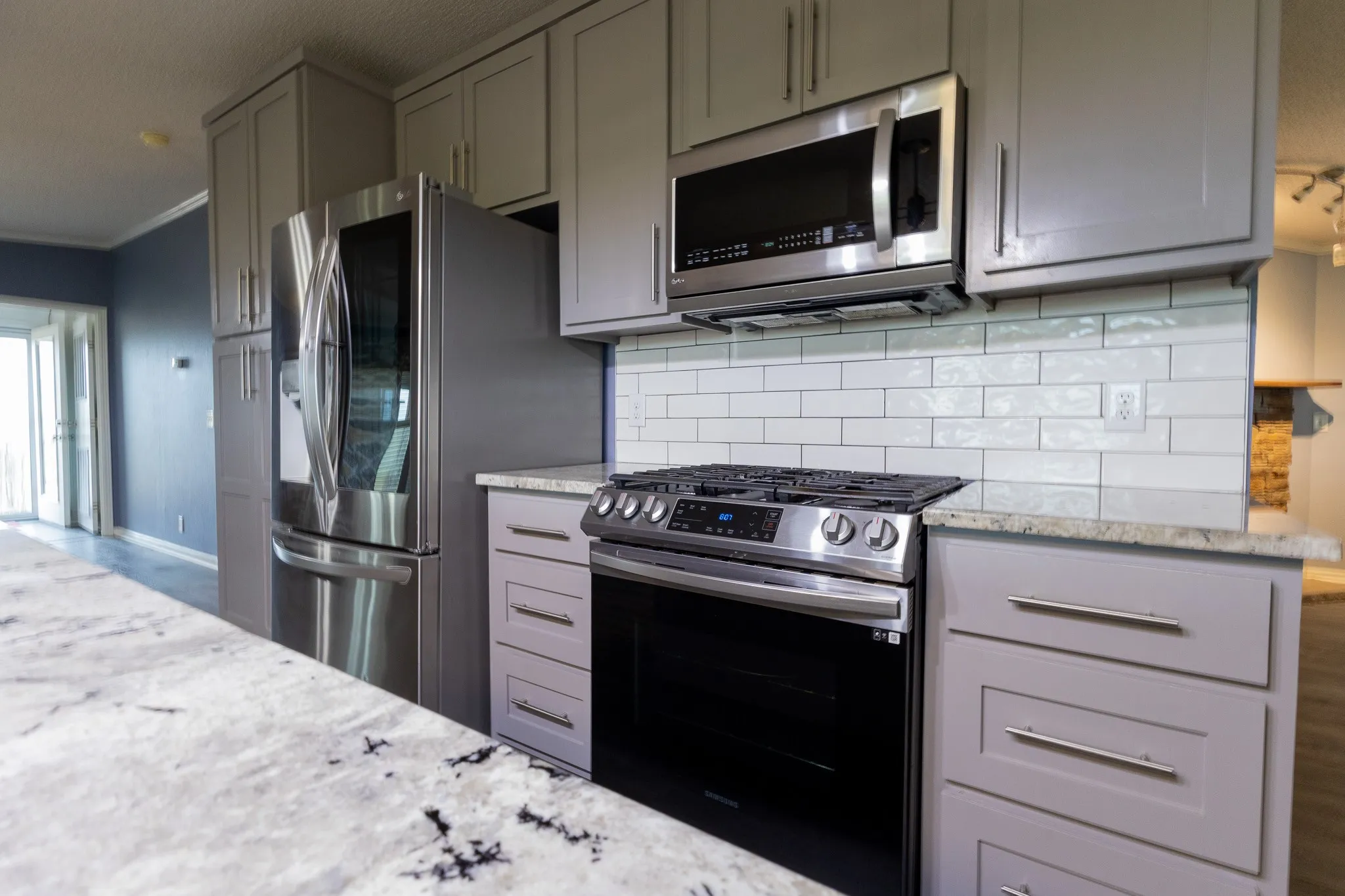 Kitchen featuring light gray cabinetry with brushed nickel hardware, stainless steel appliances, white subway tile backsplash, and light-toned countertops