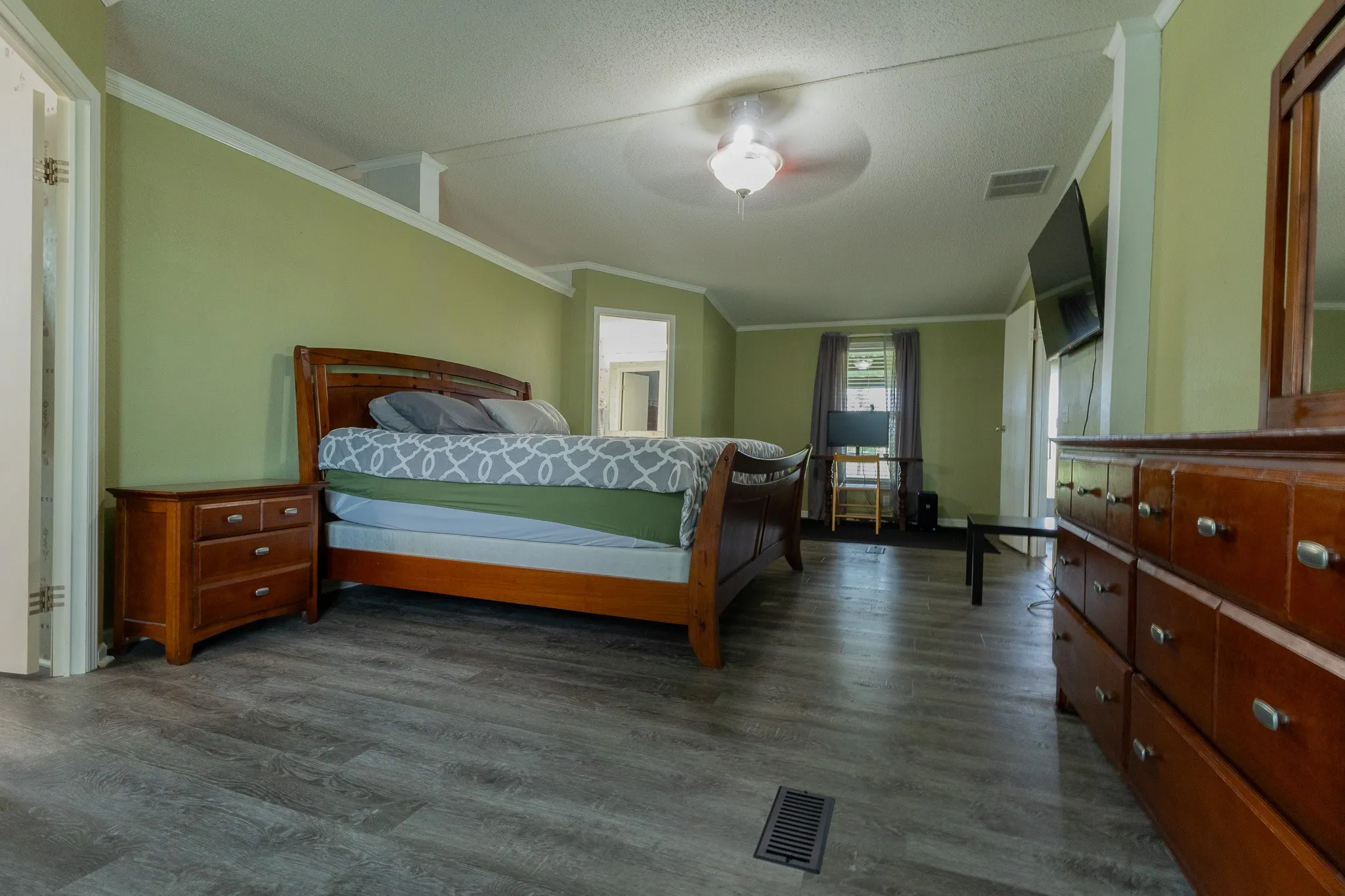 Spacious room featuring wood-finish flooring, a ceiling fan with integrated lighting, and light green walls with white trim