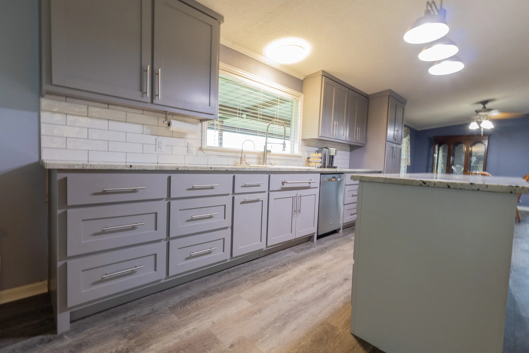 Kitchen featuring a white subway tile backsplash, light gray cabinetry, light-toned countertops, wood-finish flooring, and a center island