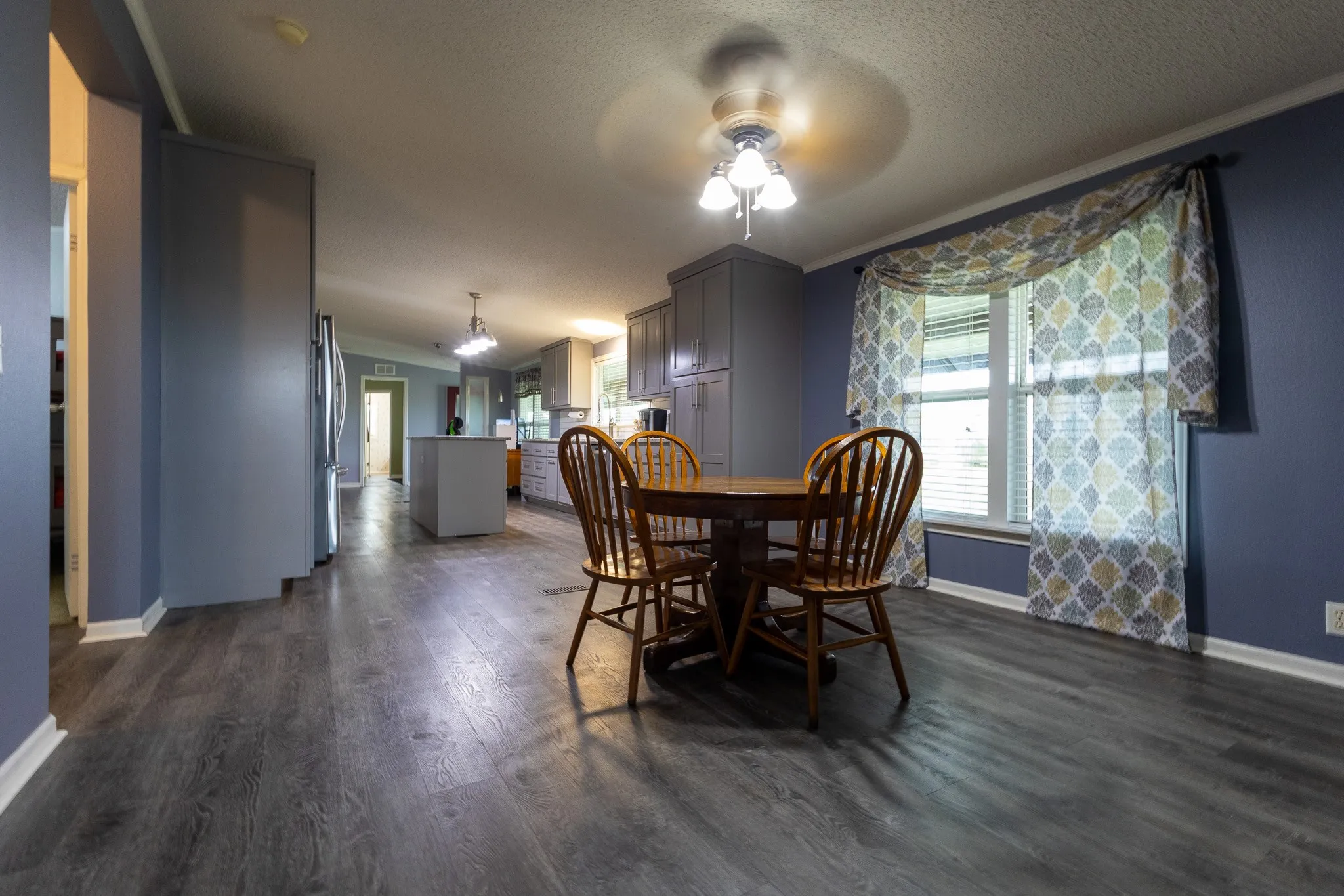 Expansive dining area featuring wood-finish flooring, a ceiling fan with integrated lighting, and a window with blinds
